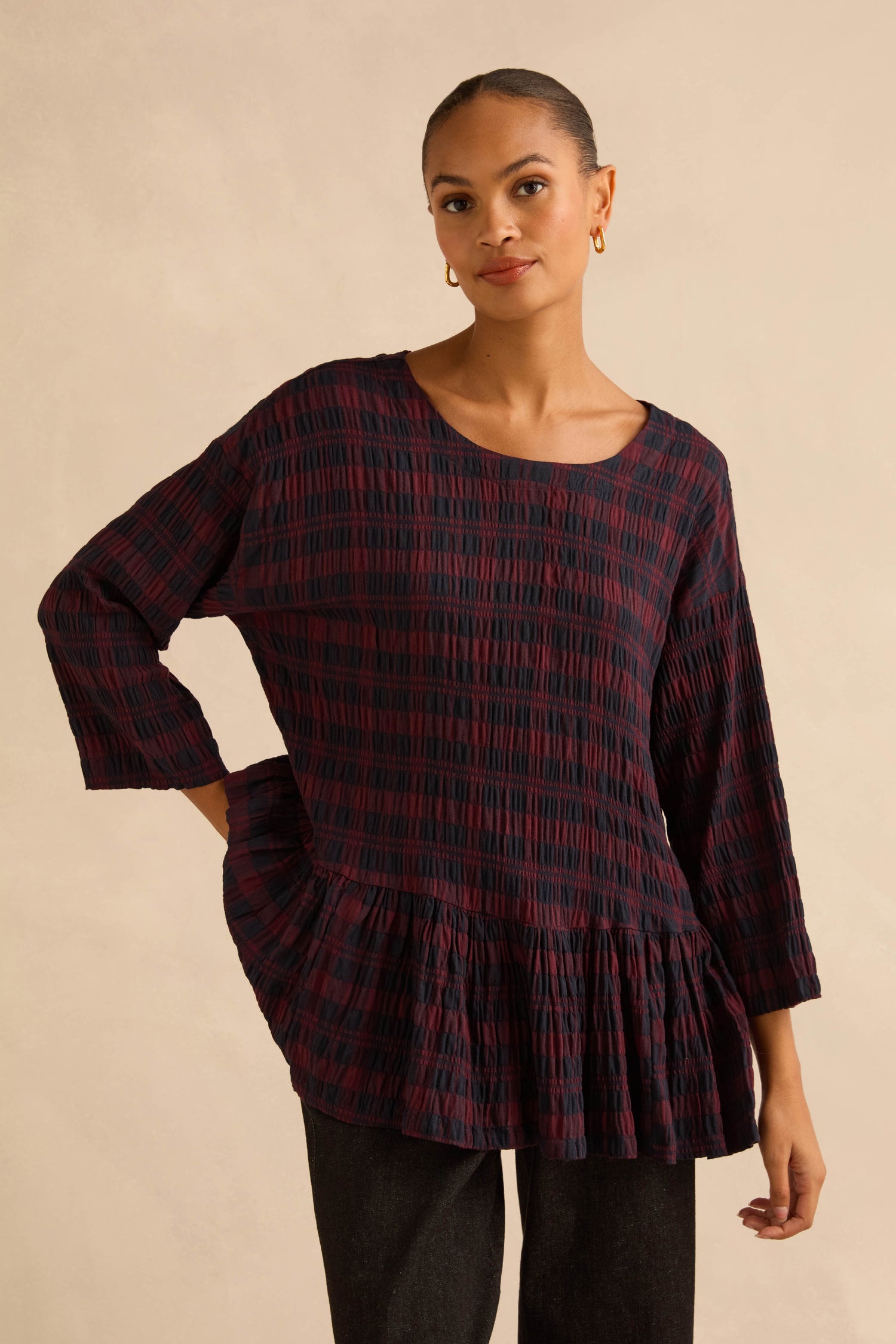 A model wears a dark red and black Crinkle Check Frill Hem Top, featuring long sleeves and a ruffled peplum hem.