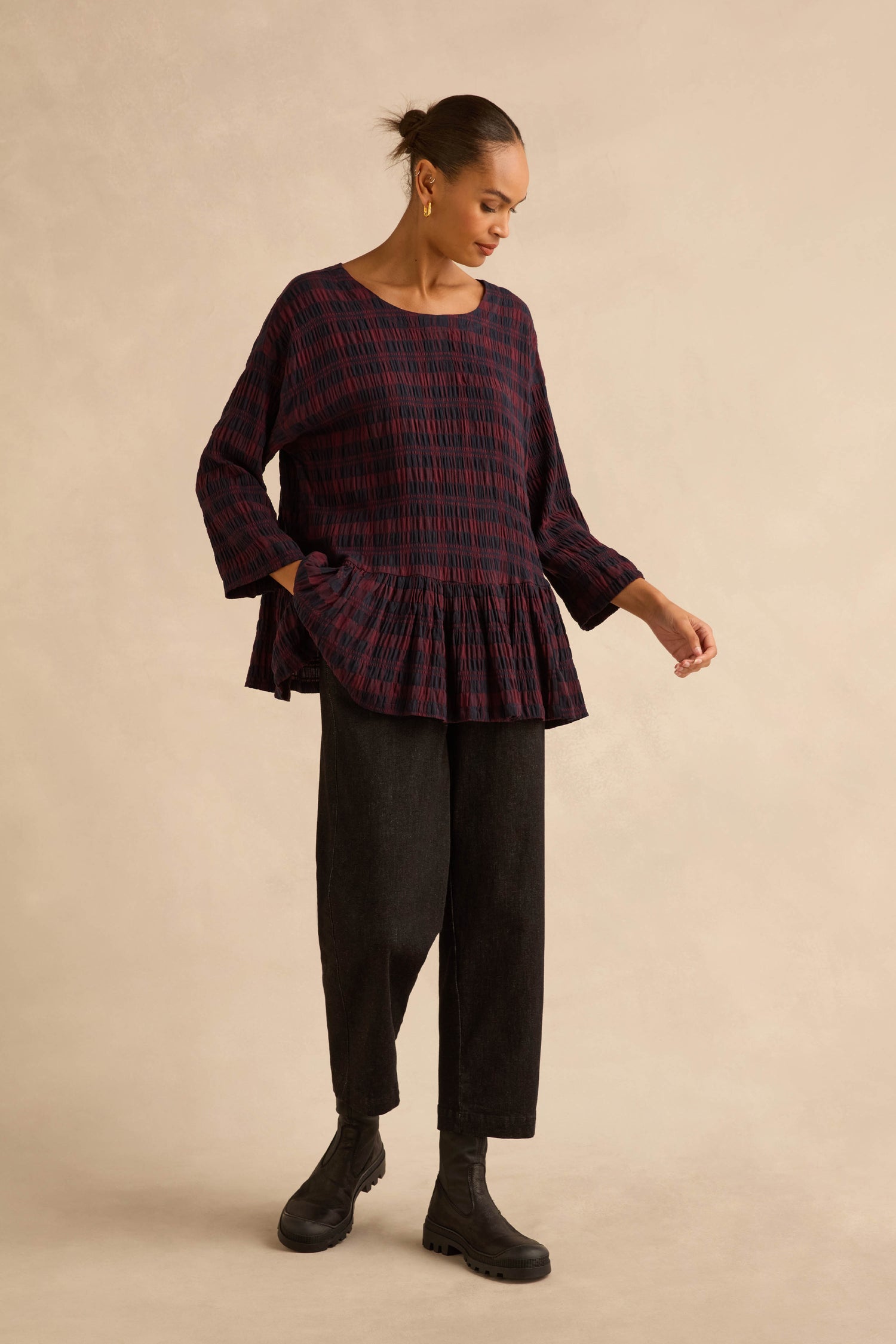 A person wearing a Crinkle Check Frill Hem Top in dark red and navy blue, paired with black trousers and black ankle boots.