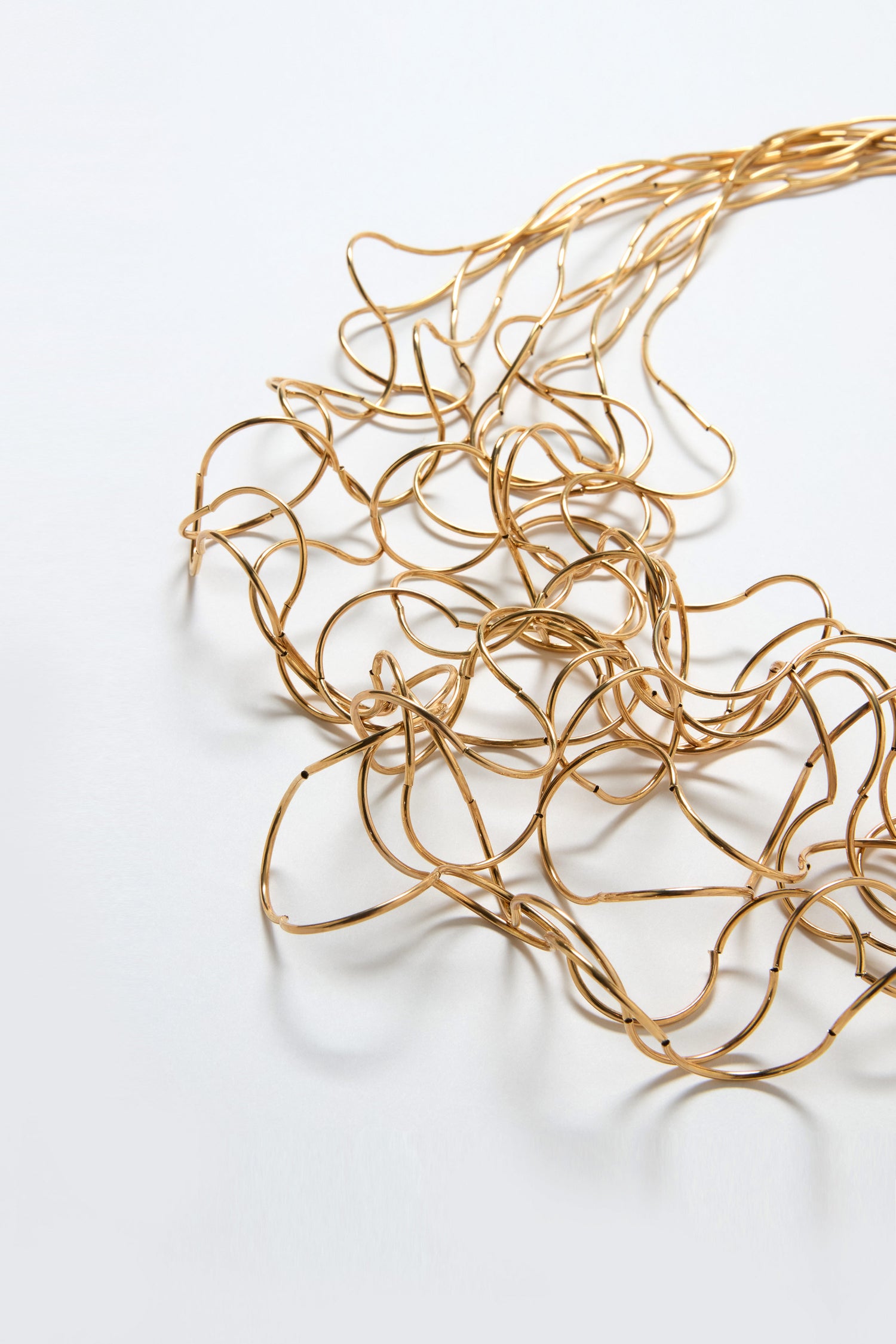 The Long Medley Necklace, a loosely coiled gold metallic piece with sculptural elegance, is displayed on a white surface.