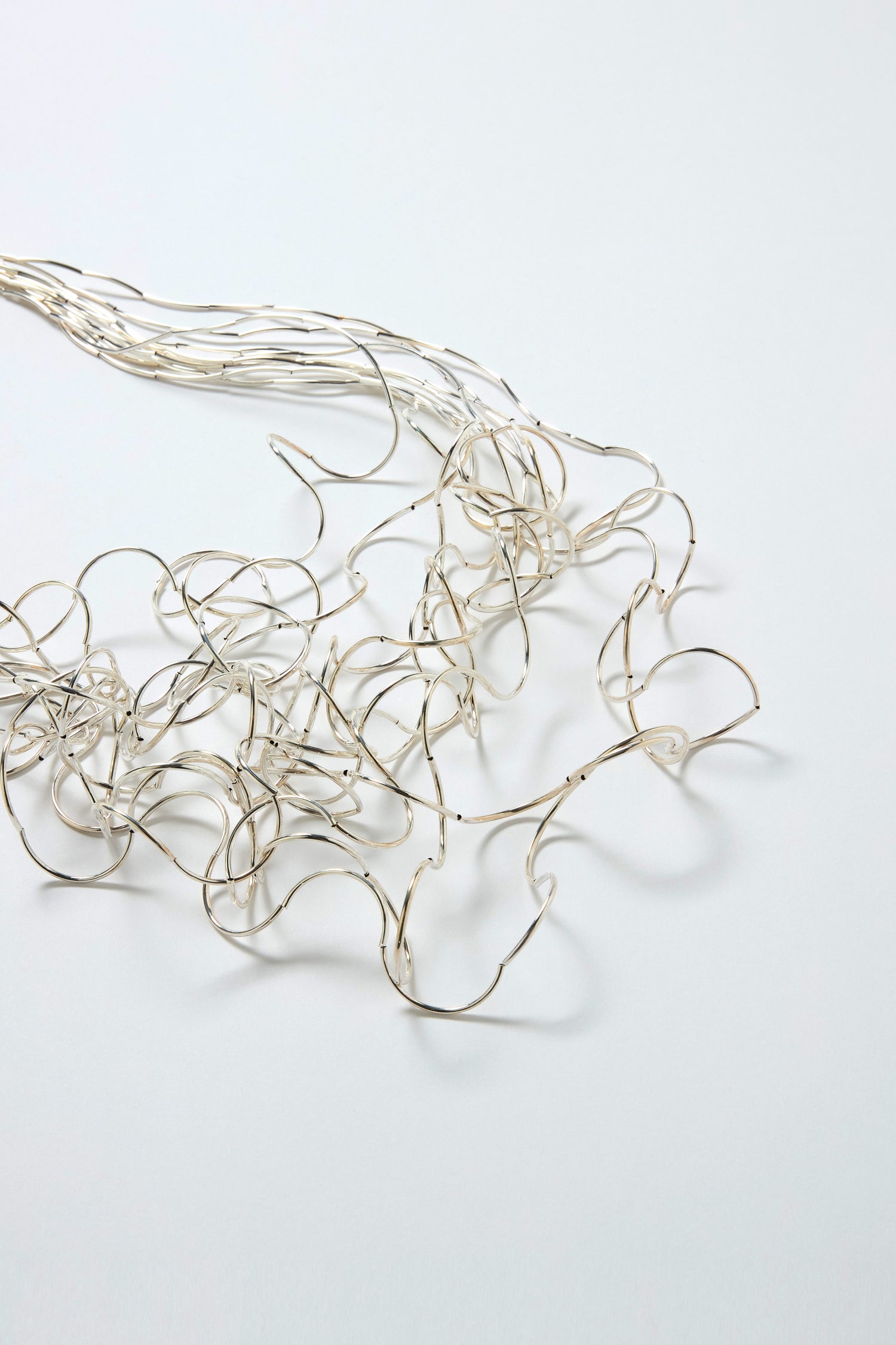 The Long Medley Necklace, featuring a bundle of thin, silver multi-strand wires, is artfully tangled and spread out on a plain white surface, creating an impression of sculptural elegance.