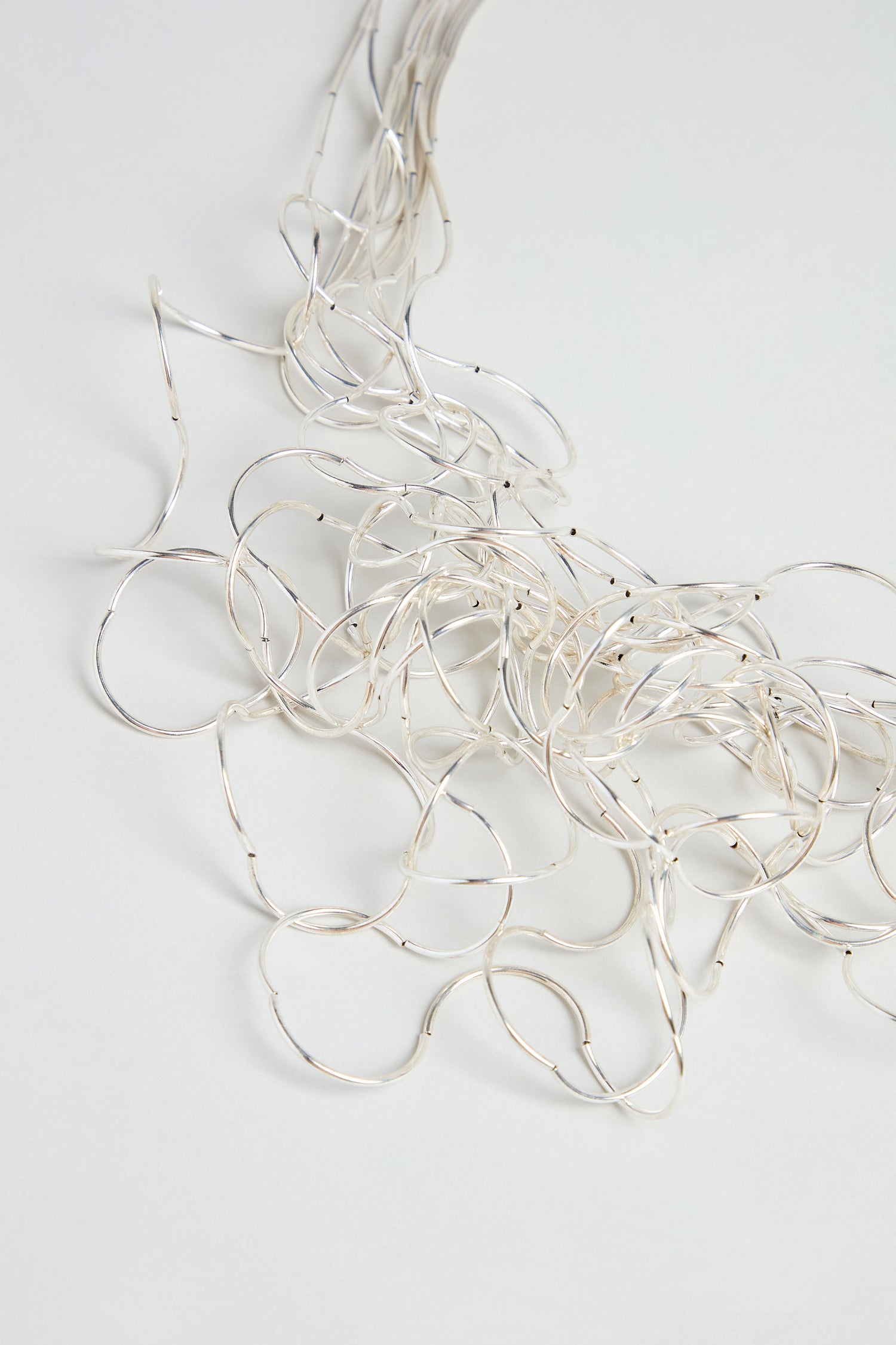 A Silver Long Medley Necklace, with its delicate strands of thin silver wires, is spread out on a light gray surface.