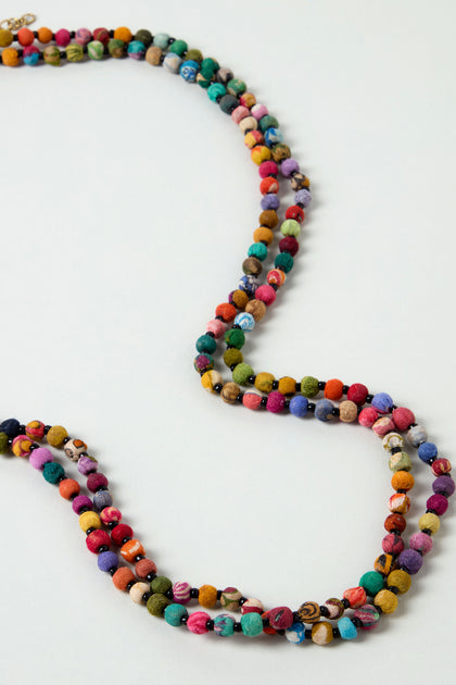 The Kantha Long Bead Spheres Necklace showcases multiple strands of handmade bead spheres crafted from recycled cotton, arranged loosely on a plain light surface.