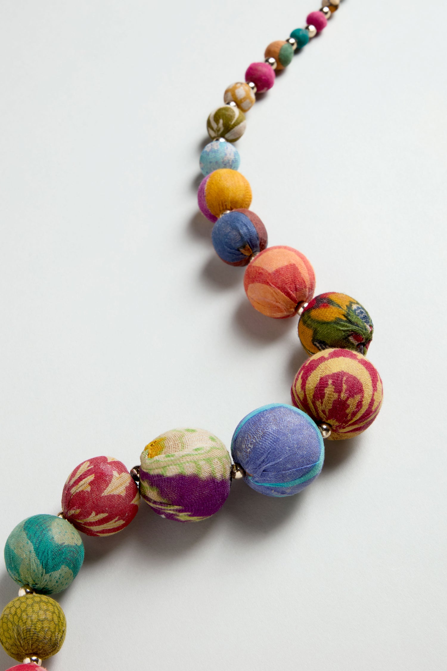 The Kantha Graduated Bead Necklace features colorful, patterned beads made from recycled cotton fabric, beautifully handcrafted and displayed on a light surface.