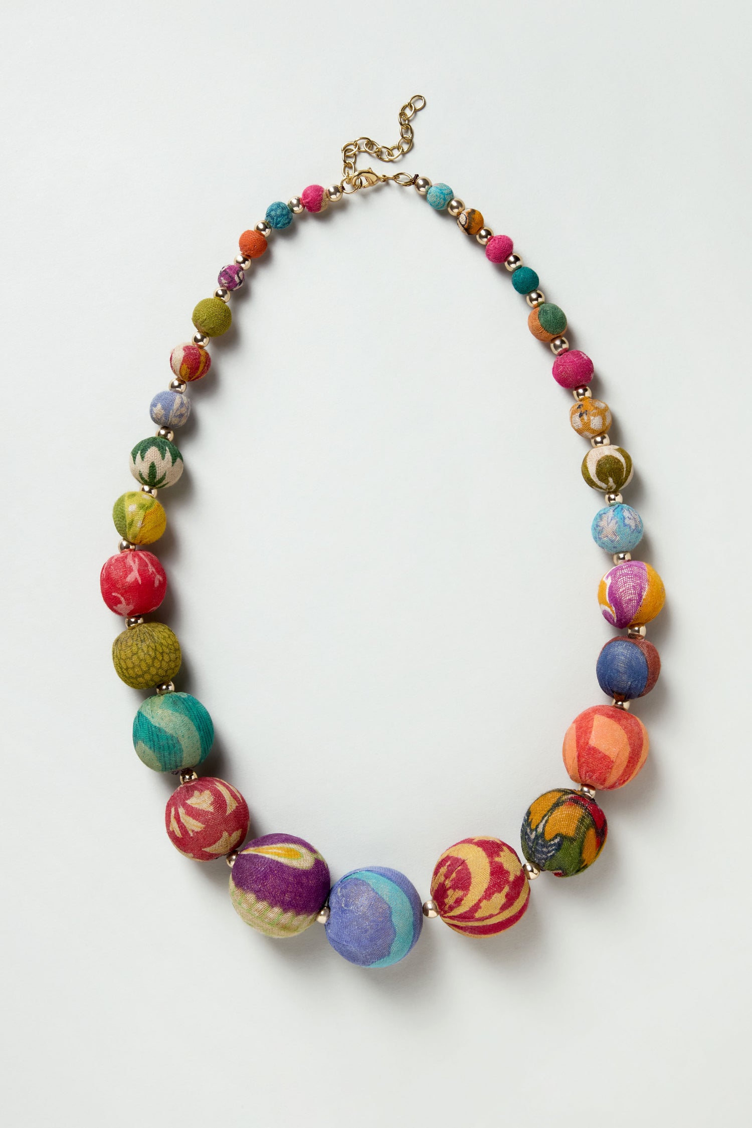 The Kantha Graduated Bead Necklace showcases large, round, multicolored patterned beads made from recycled cotton, finished with a gold chain clasp and displayed on a white background.