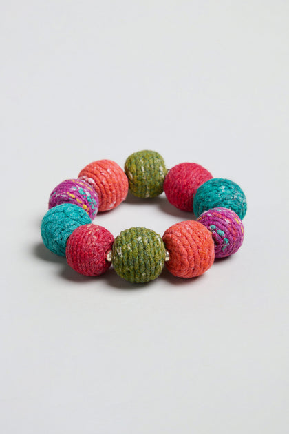 The Rainbow Kantha Spheres Bracelet features large, round, multicolored textured beads in orange, green, teal, pink, and purple arranged in a circle on a plain background. Each cotton-wrapped wooden bead makes this statement bracelet both eye-catching and unique.