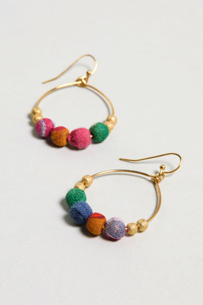 The Kantha Gilded Hoop Earrings feature multicolored fabric-wrapped beads made from recycled cotton and small textured gold beads, shown on a light surface.