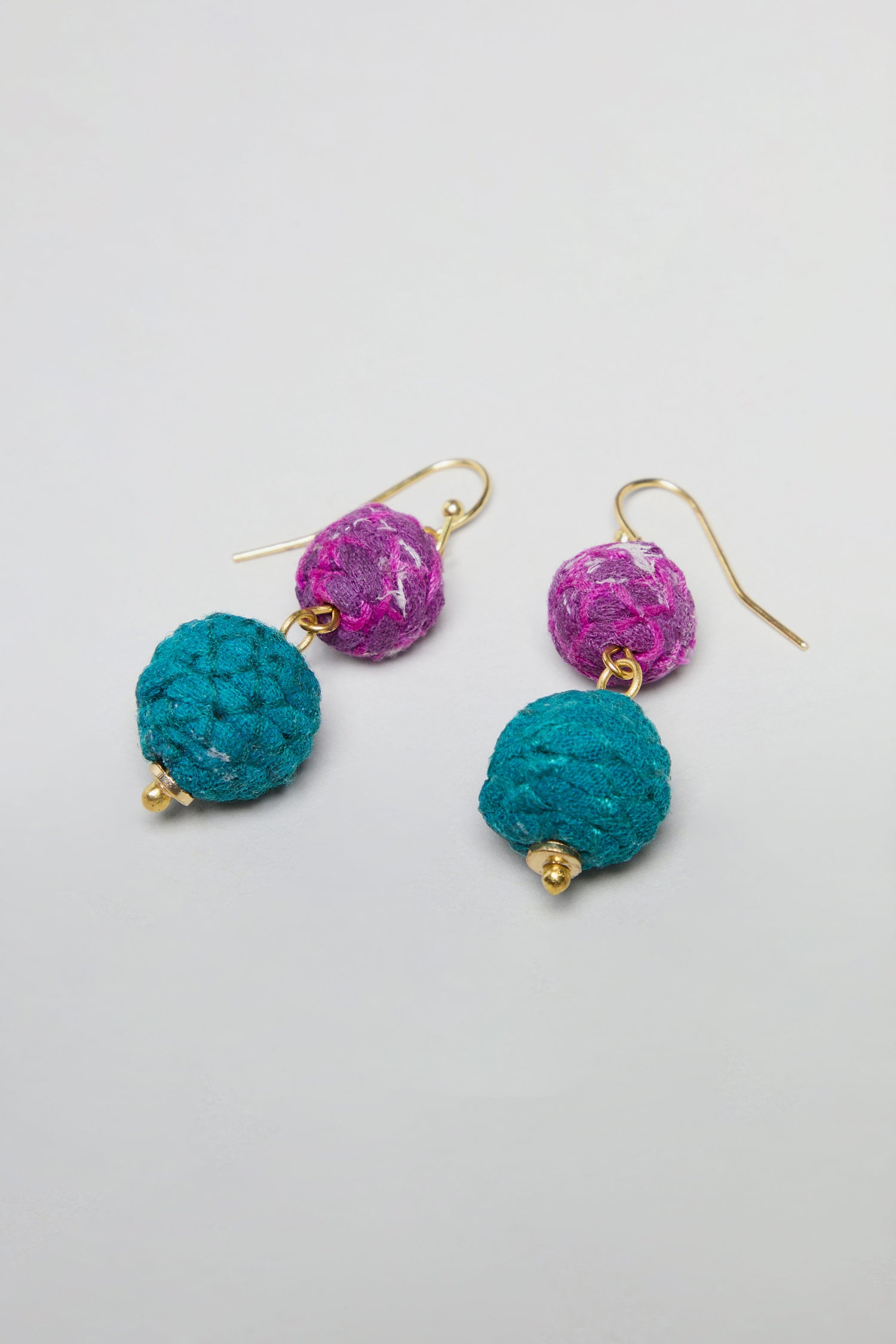 The Kantha Double Spheres Earrings feature gold hooks with a purple cotton-wrapped bead stacked above a larger teal textured bead, shown against a plain white background.