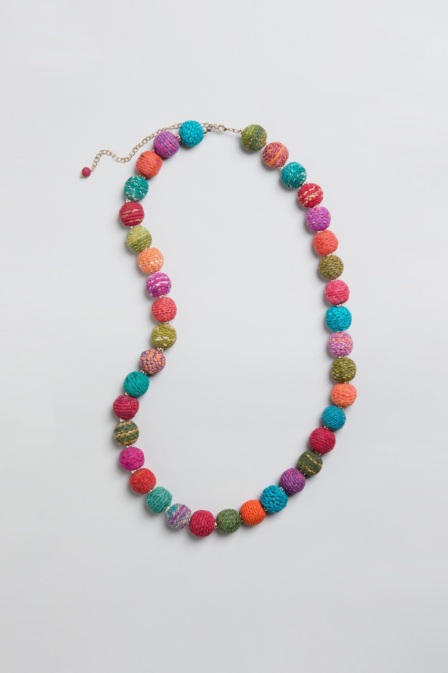 The Rainbow Kantha Spheres Necklace showcases multicolored, textured round cotton-wrapped beads that are evenly spaced along a thin chain and set against a light gray background—making it a vibrant example of rainbow jewelry.