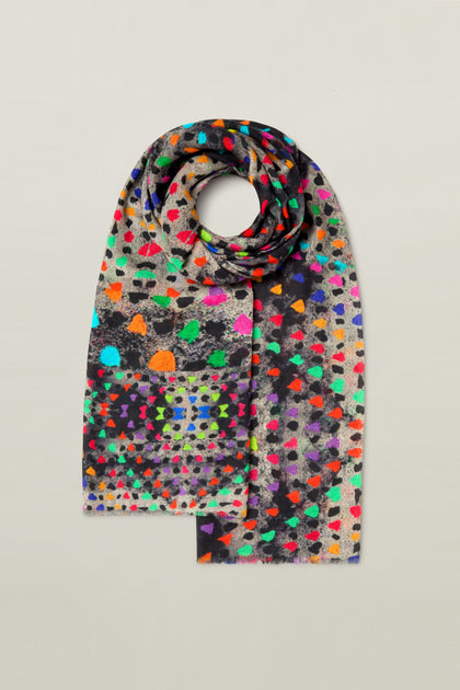 A Painted Triangles Wool Scarf features a multicolored abstract dotted pattern and a rainbow triangle print, displayed against a plain background.