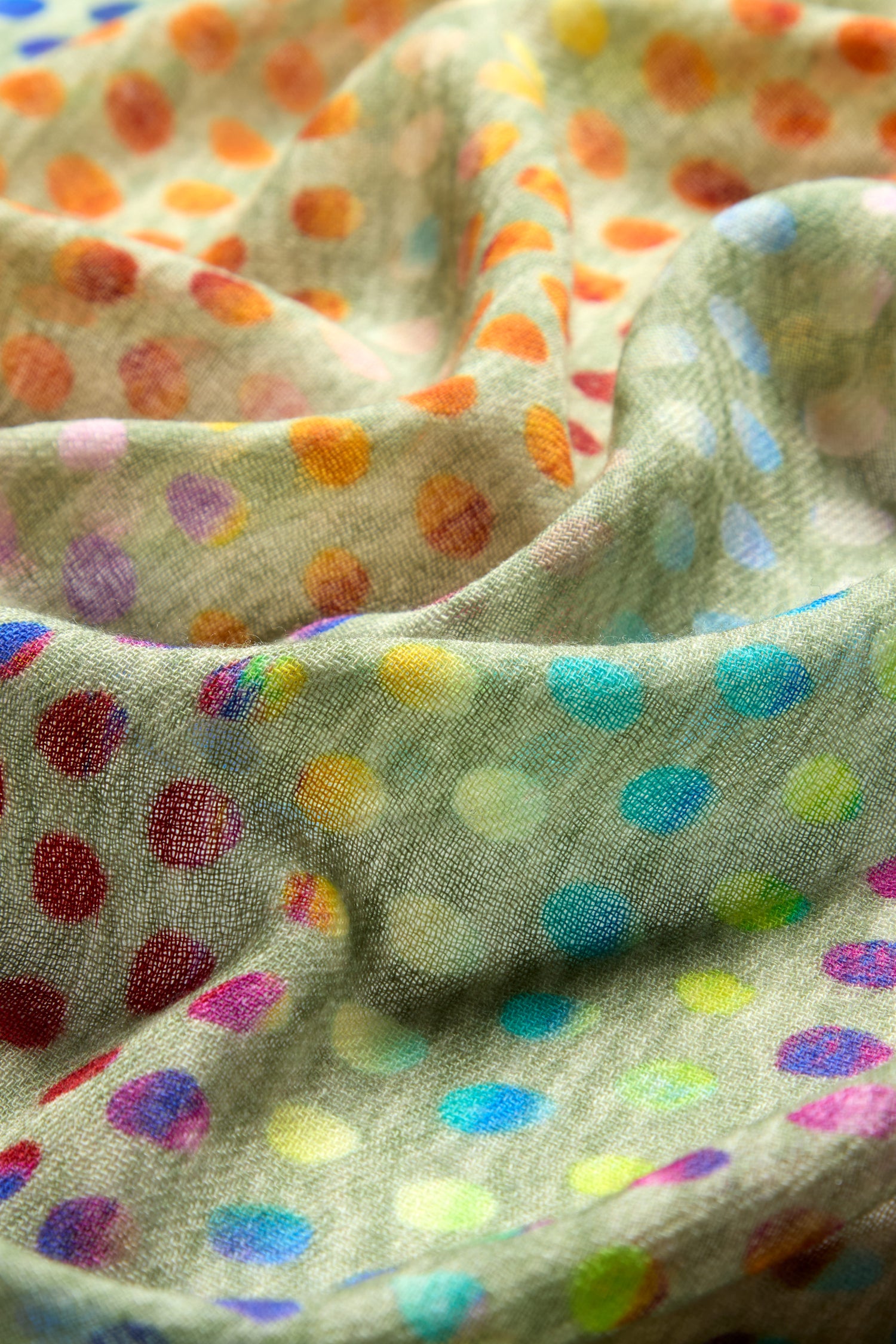 Close-up of the Mini Rainbow Spot Merino Wool Scarf, showcasing its textured fabric adorned with colorful polka dots in various shades and sizes on a light background.