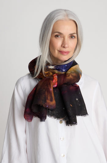 A woman with long gray hair wearing a white shirt and a Cosmic Sky Print Wool Scarf stands against a plain background.