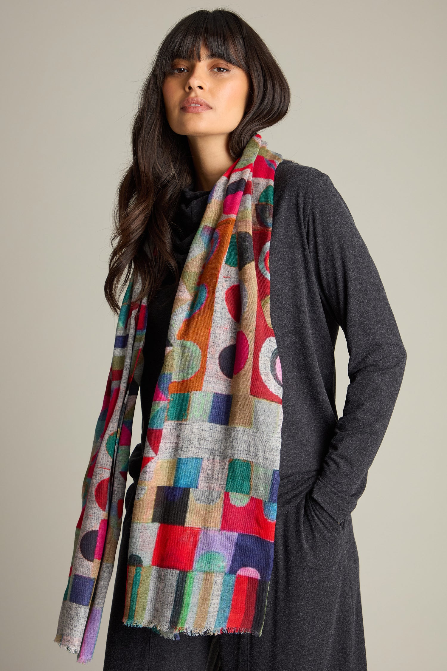 Person wearing a Kandinsky Merino Wool Scarf featuring vibrant geometric patterns over a dark grey dress, standing against a neutral background.