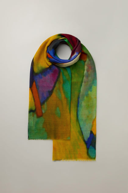 The Painterly Wool Blend Scarf, featuring a multicolored tie-dye pattern in vibrant blue, green, yellow, and red hues, is elegantly displayed on a white background—perfect for versatile styling.