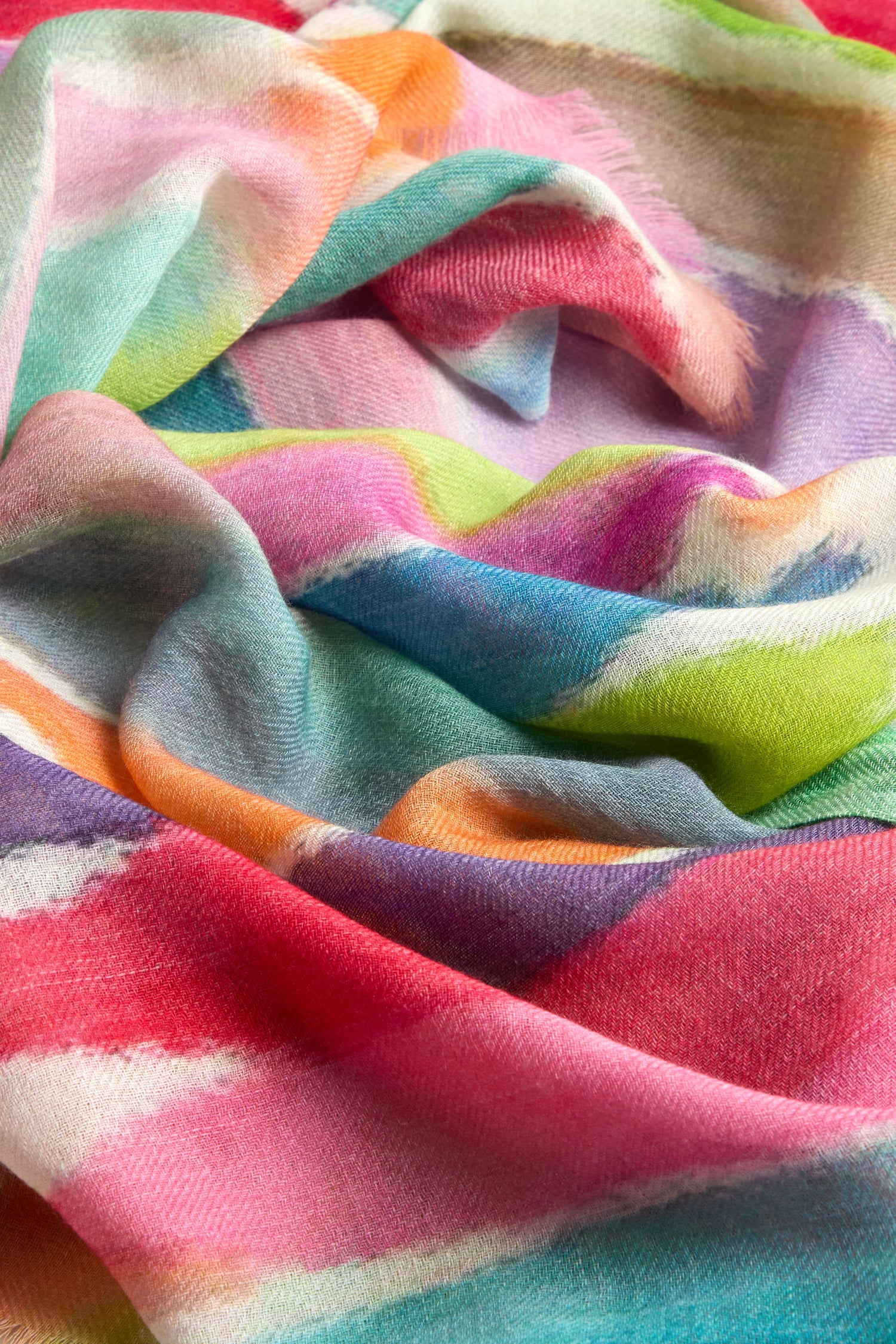 A close-up of the Shaded Watercolour Stripe Wool Blend Scarf, showcasing a crumpled wool blend with a tie-dye pattern in shades of pink, blue, green, orange, and white.