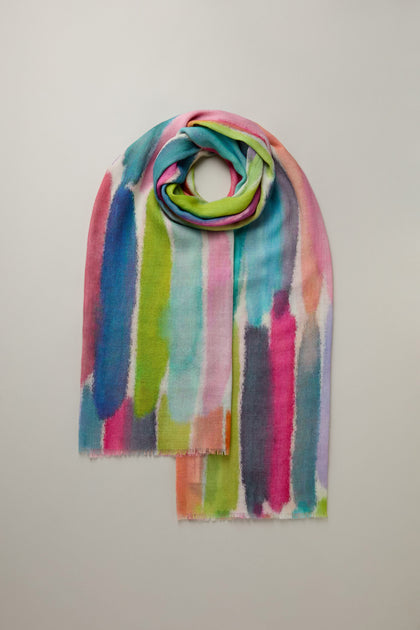 Explore the Shaded Watercolour Stripe Wool Blend Scarf, featuring a vibrant palette of pink, orange, blue, green, and white stripes. This lightweight accessory adds an elegant touch to any wardrobe and is beautifully displayed against a plain white background.