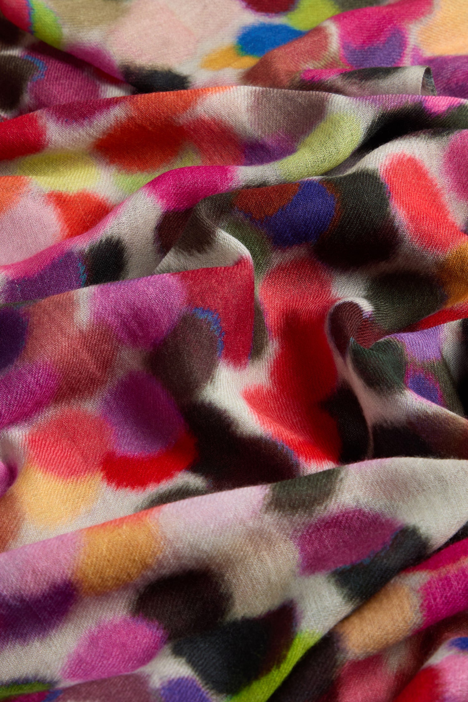 The Dotty About You Wool Blend Scarf features a colorful, abstract pattern with dotted designs in red, pink, purple, blue, green, and black hues. Its soft texture offers an inviting and vibrant visual experience.