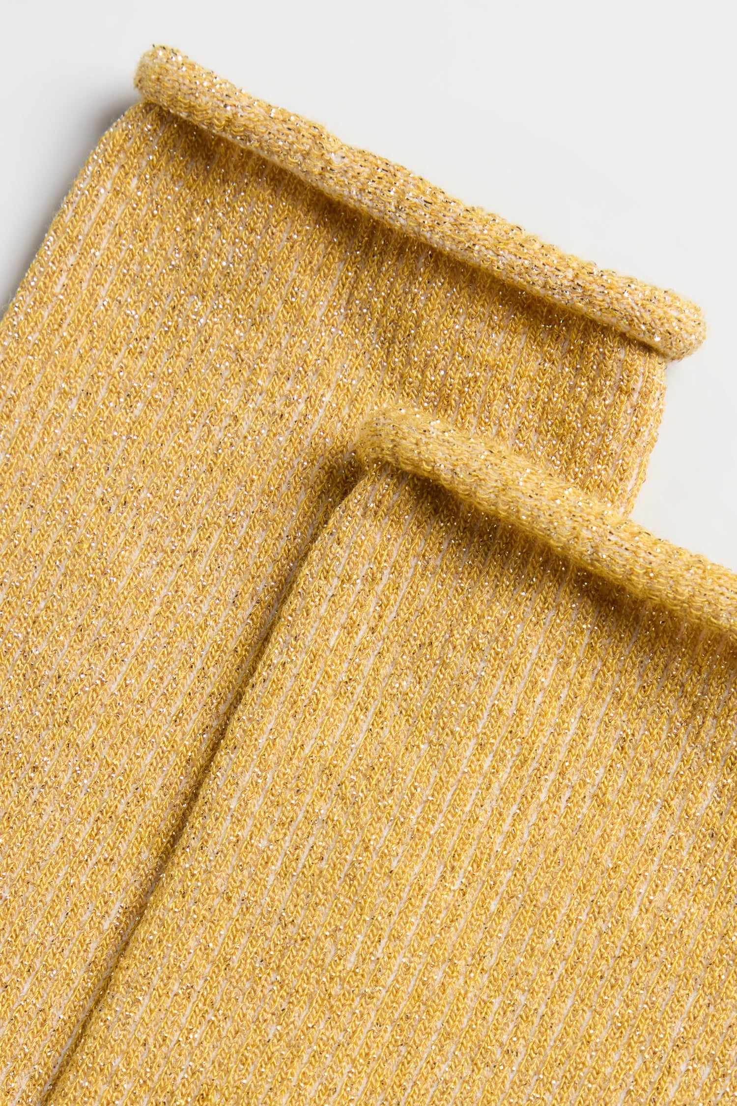Close-up of two Bamboo Sparkle Dijon Socks, featuring rolled edges and a gold metallic lurex sheen, lying flat on a white surface.