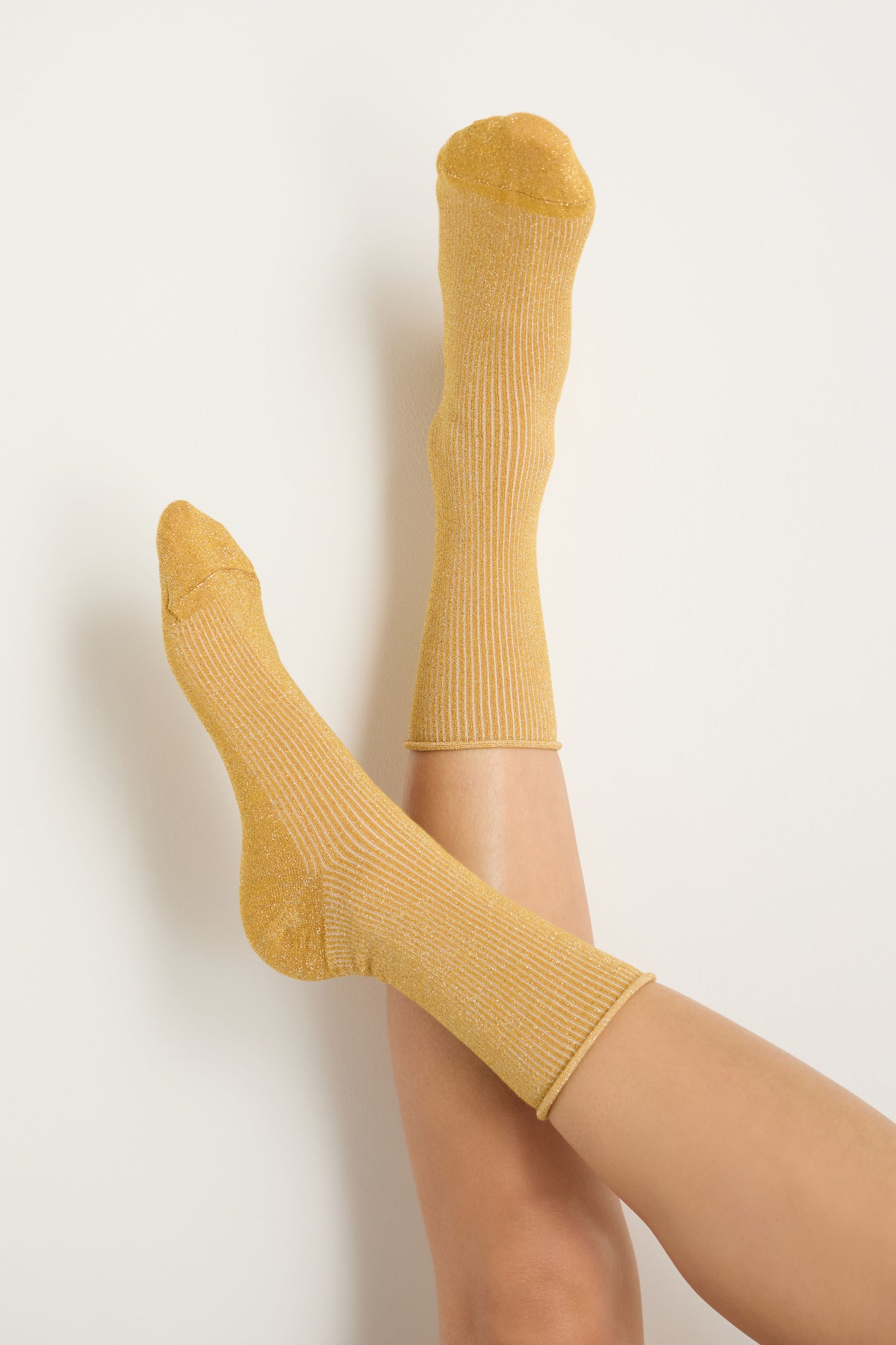 A person with bare legs wears Bamboo Sparkle Dijon Socks, legs crossed and raised against a plain white background.