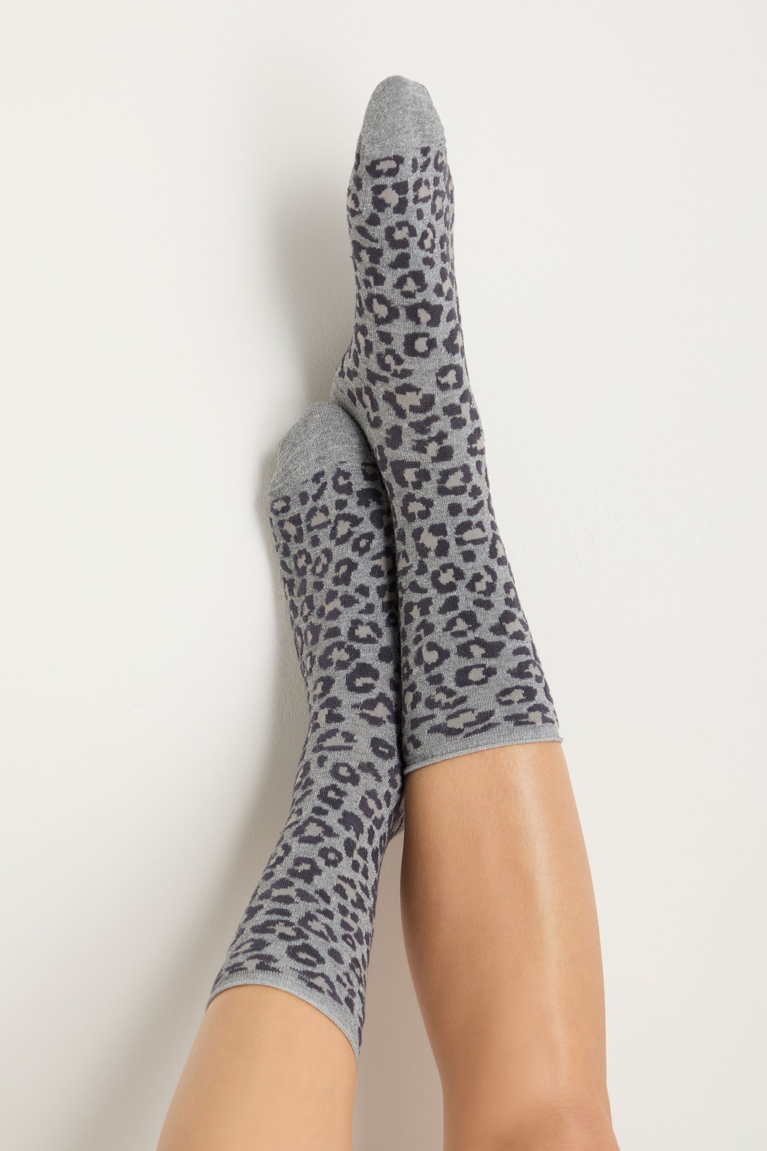 Person wearing Bamboo Leopard Print Socks in gray, feet crossed and resting against a white background.
