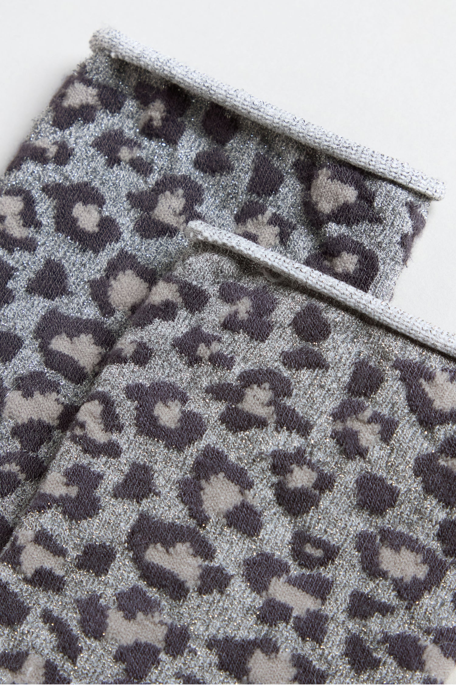 Two folded pieces of fabric feature a grey and black leopard print with metallic threads, ideal for creating stylish Bamboo Leopard Print Socks.