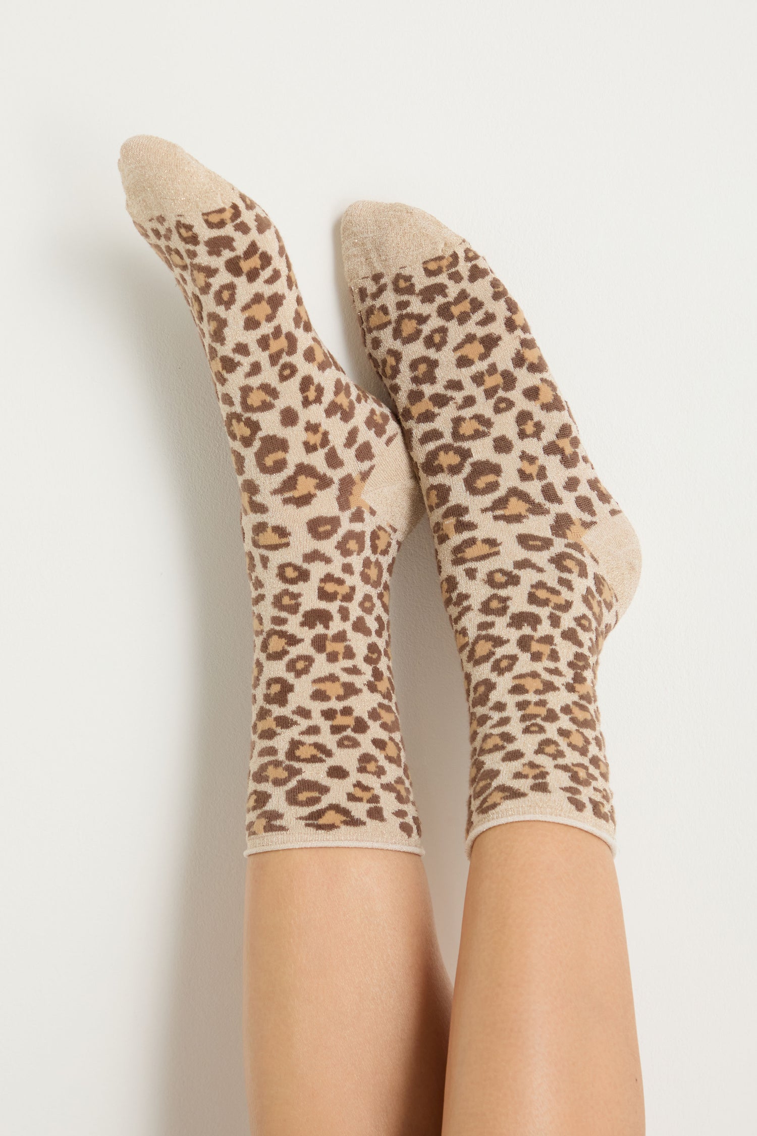 A pair of feet wearing Bamboo Leopard Print Socks with a beige, brown, and black pattern, set against a plain white background.