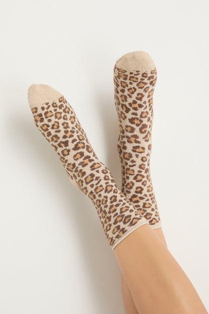 A pair of feet wear Bamboo Leopard Print Socks—beige bamboo-blend with a brown and black leopard pattern—shown against a plain light background.
