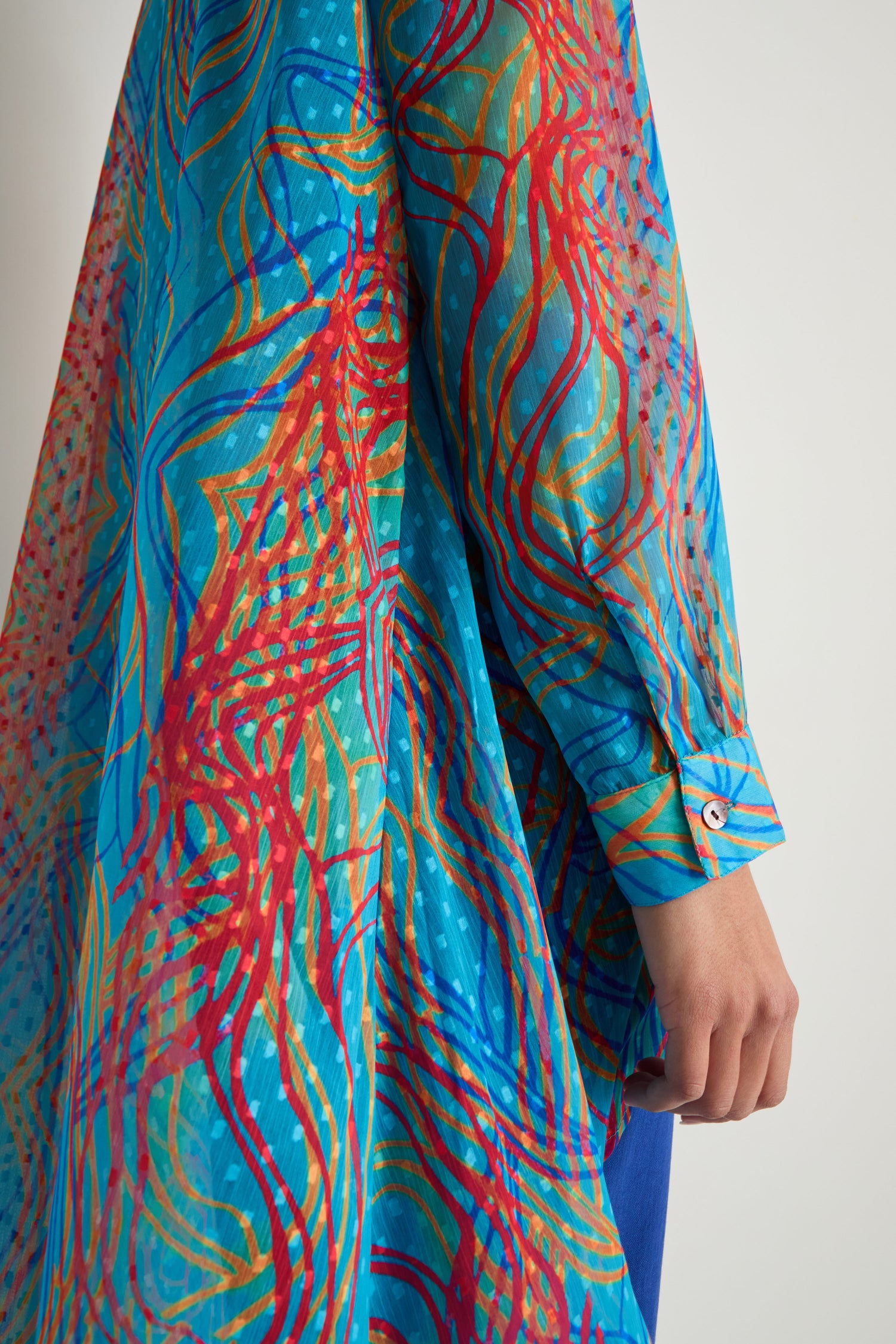 Someone wears the Twirl Print Dobby Shirt with loose, long sleeves and a vibrant abstract pattern in blue, red, and orange; only their arm and side are shown.