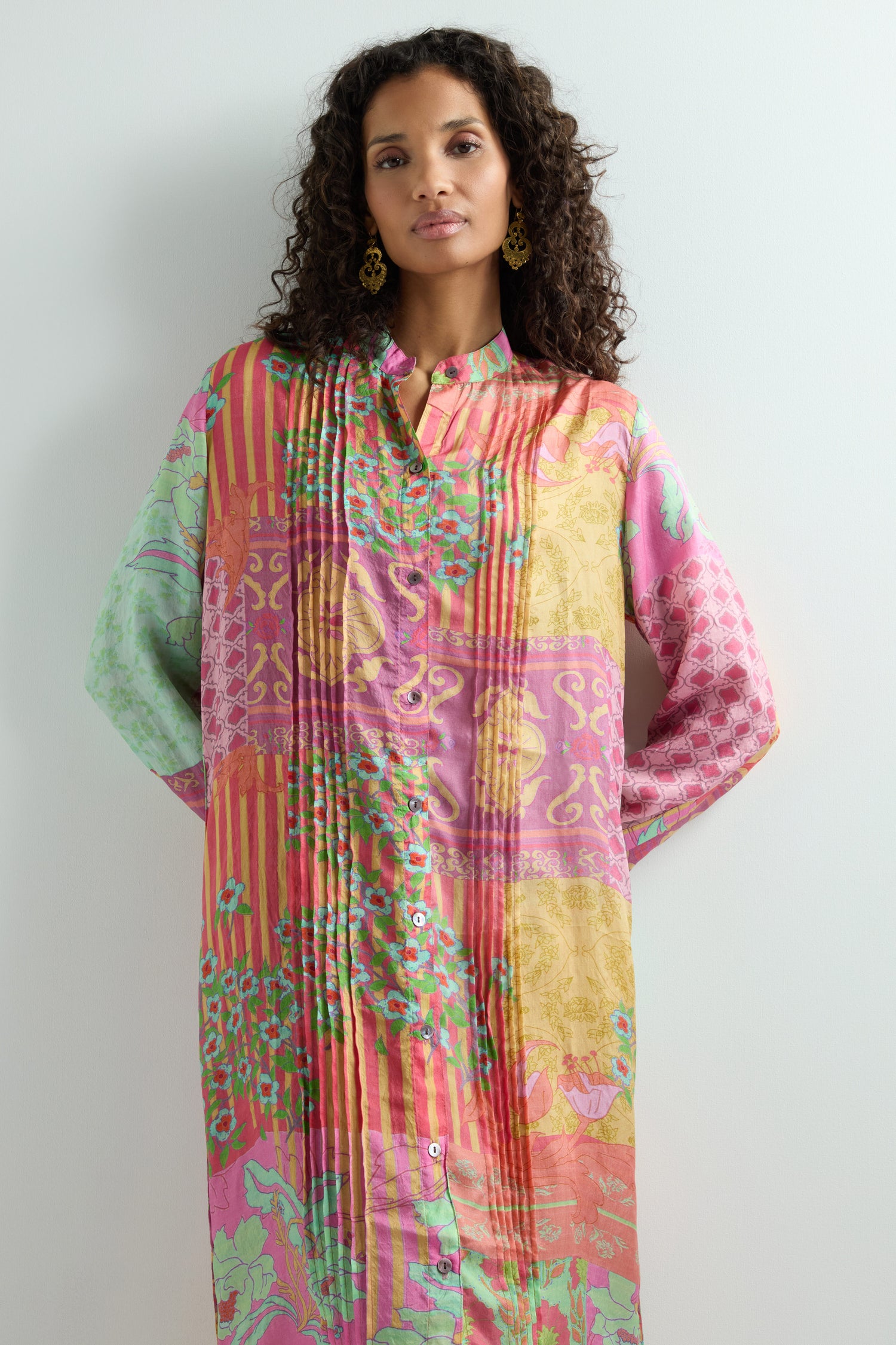 Against a plain backdrop, someone stands elegantly wearing the Geometric Floral Silk Shirt Dress, featuring a mandarin collar and vibrant design.