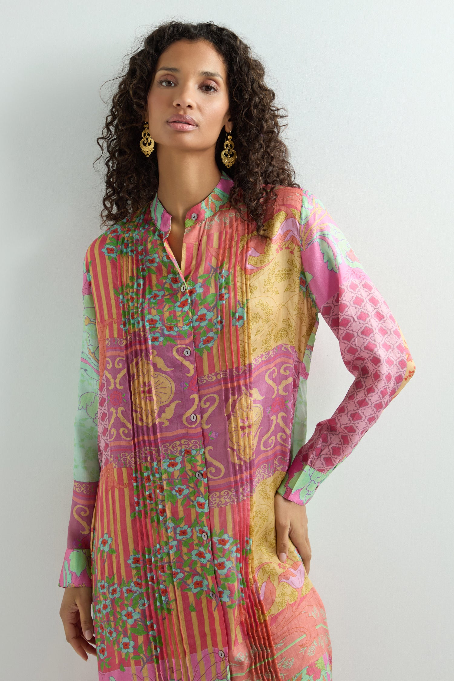 A woman with curly hair poses against a light background in a vibrant Geometric Floral Silk Shirt Dress.