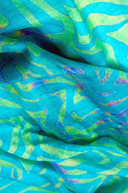 Close-up of the Ripple Silk Scarf, featuring a vibrant abstract pattern with swirling lines in shades of blue and green, accented with multicolored hints for a luxurious touch.