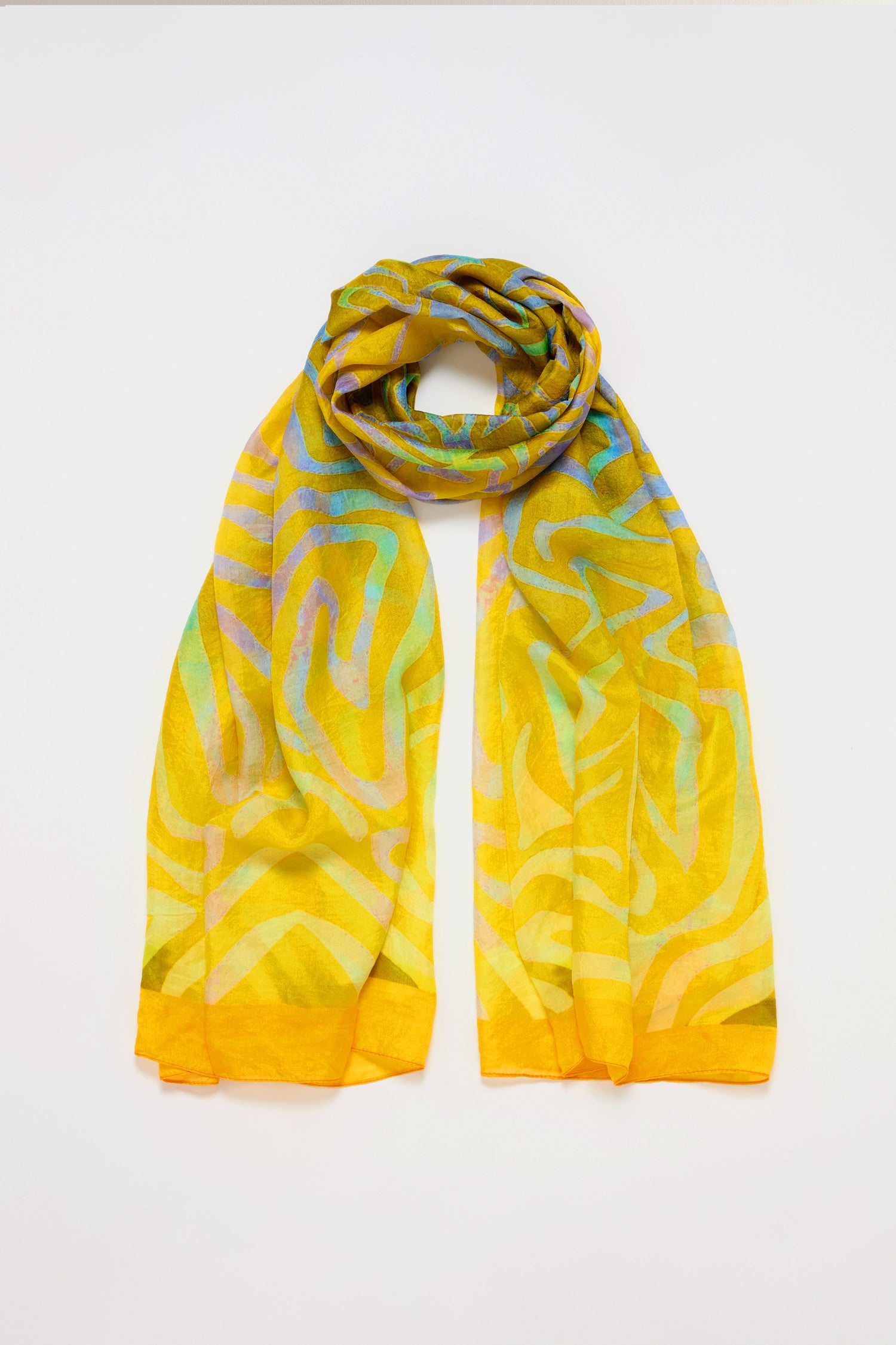 The Ripple Silk Scarf, featuring a yellow base with an abstract multicolored pattern, is elegantly looped against a white background, showcasing vibrant energy and versatile styling options.