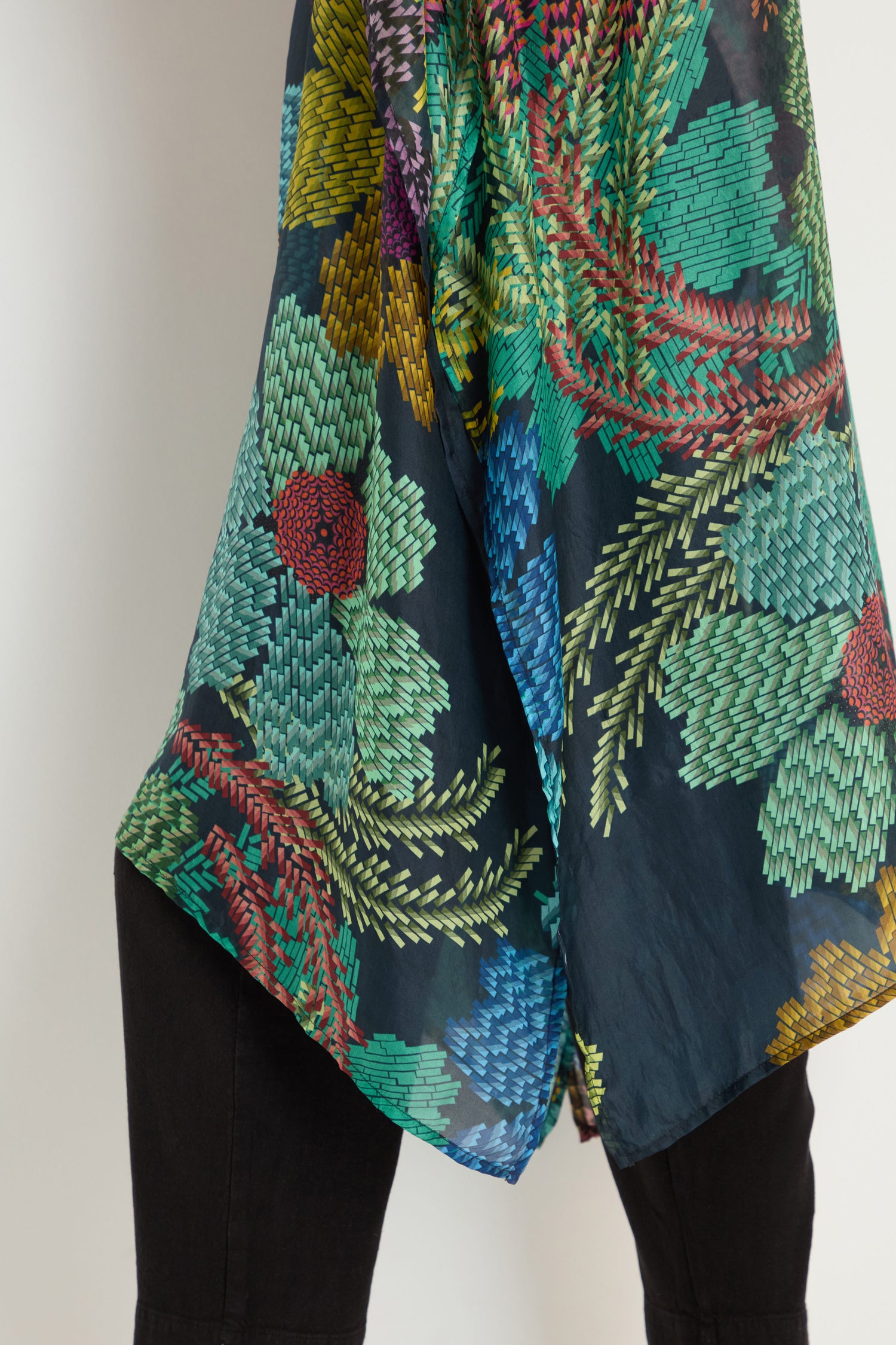 Close-up of a person wearing the Pixelated Petals Silk V-Neck Kaftan— a dark, sheer top with a colorful, pixelated floral print and foliage embroidery.