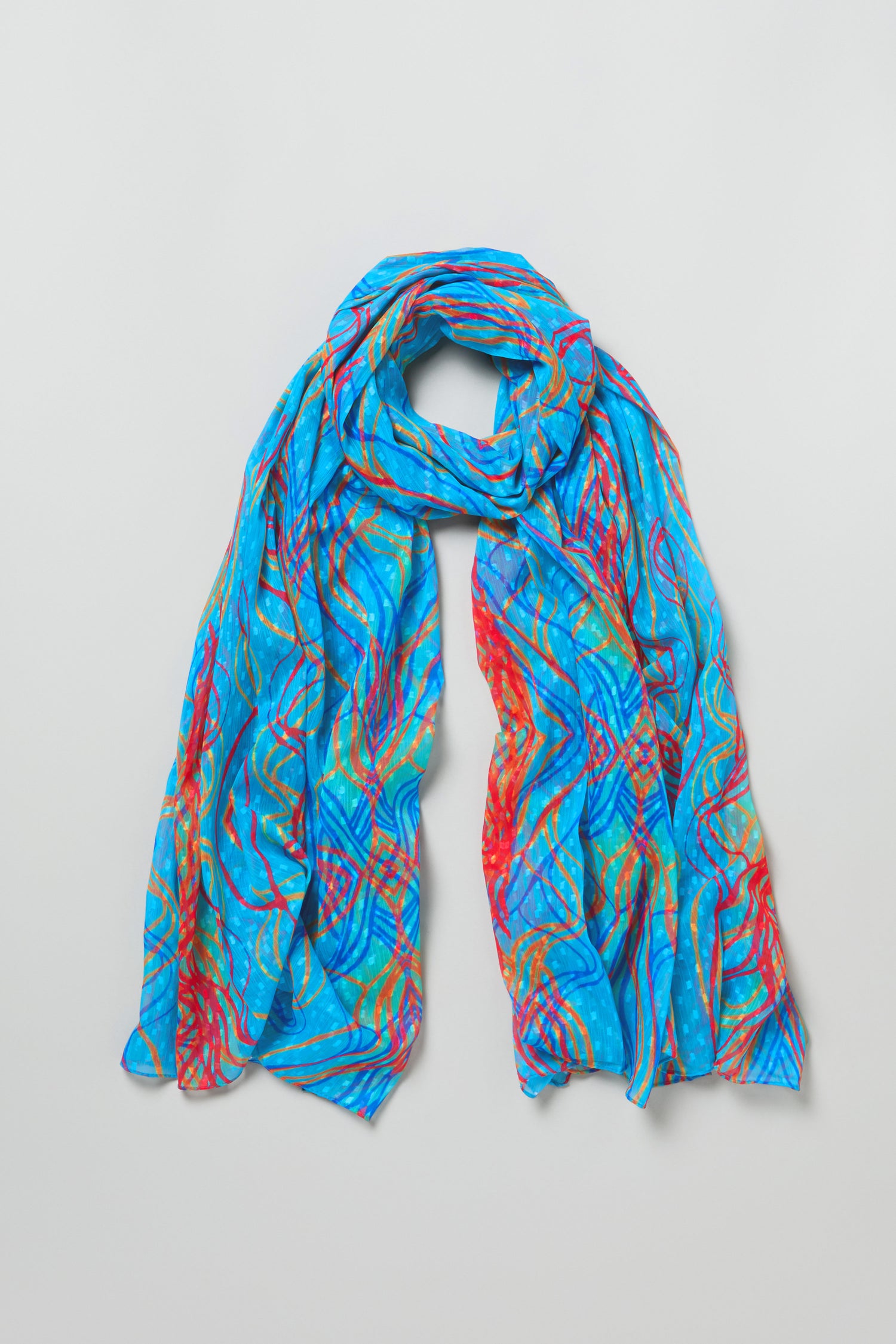 The Twirl Print Dobby Scarf features a lightweight design with a blue background and multicolored abstract swirls, displayed in loose folds on a plain light surface.