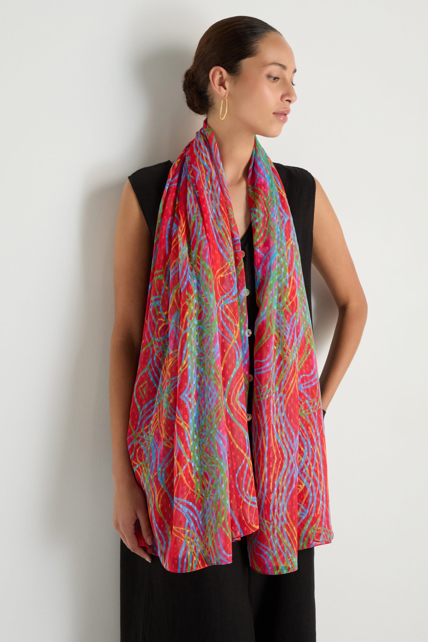 A woman in a sleeveless black dress stands against a white wall, wearing the Twirl Print Dobby Scarf draped around her neck and shoulders.