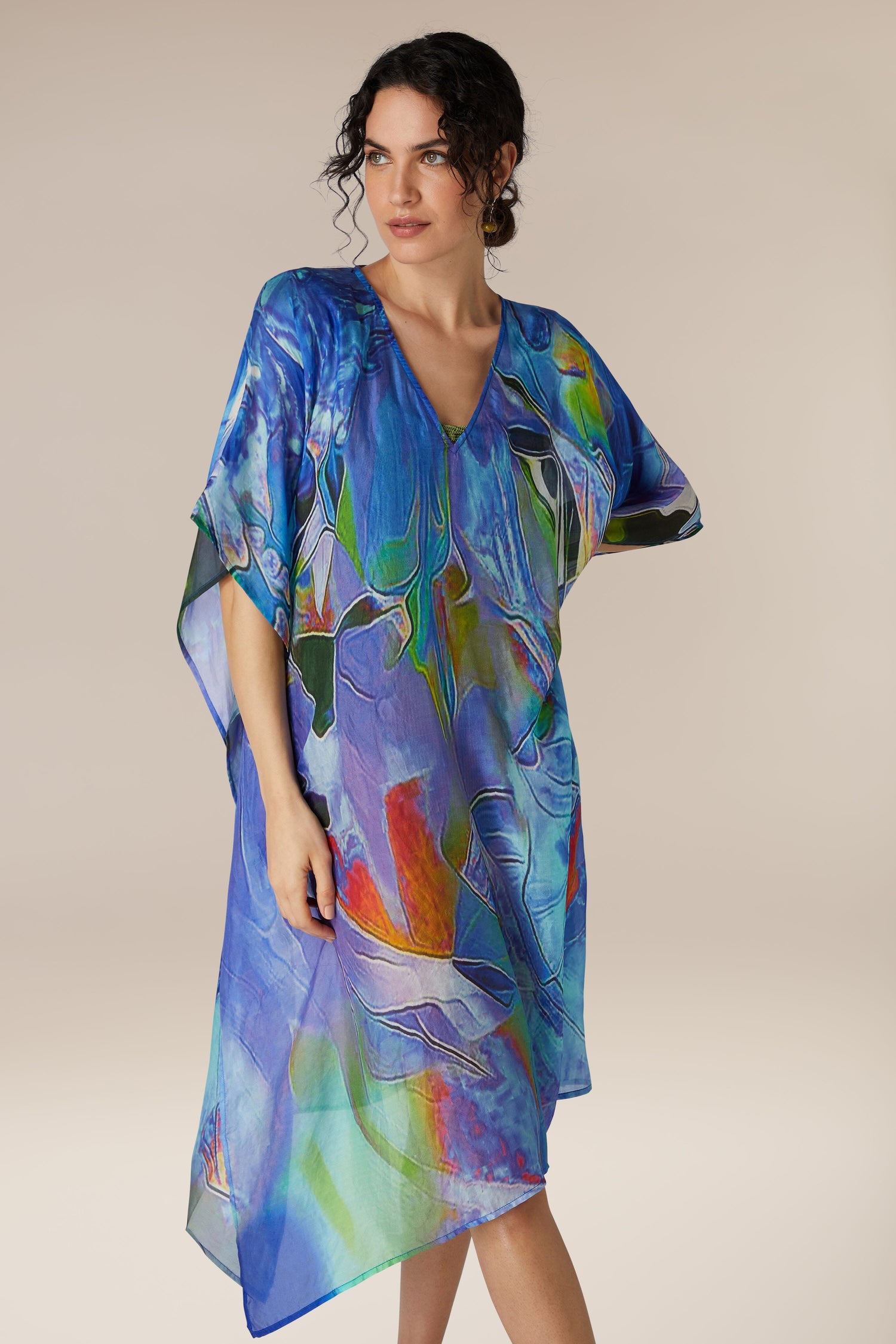 Woman wearing a colorful Tiffany Lamp Silk V Neck Kaftan as a beach cover-up against a neutral background.