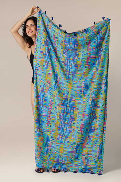 Woman playfully peeking from behind a Rainbow Wave Beach Towel.