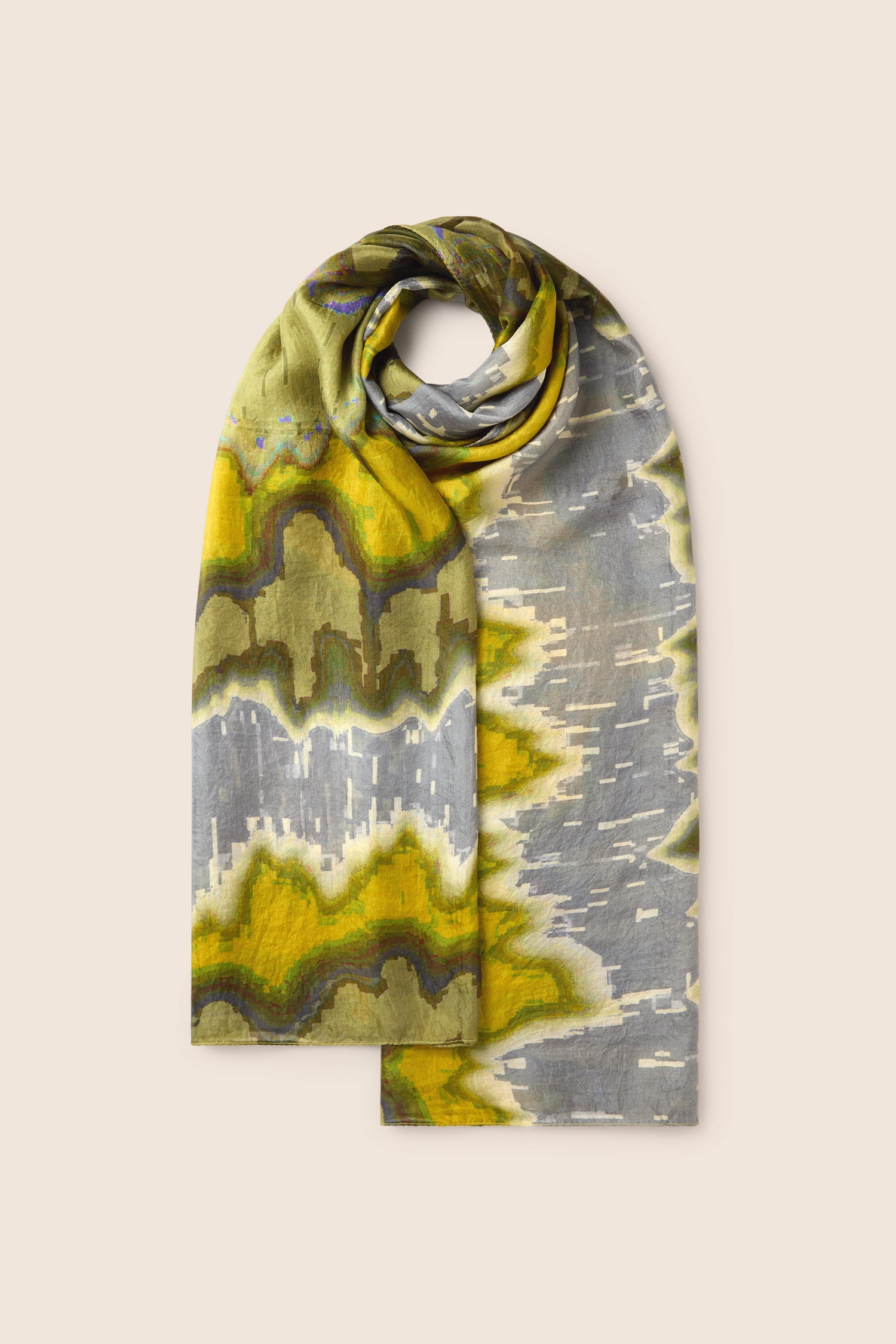 The Mineral Silk Scarf showcases expert craftsmanship, presenting a folded shawl adorned with an abstract pattern in hues of green, yellow, and gray, set against a plain beige backdrop.