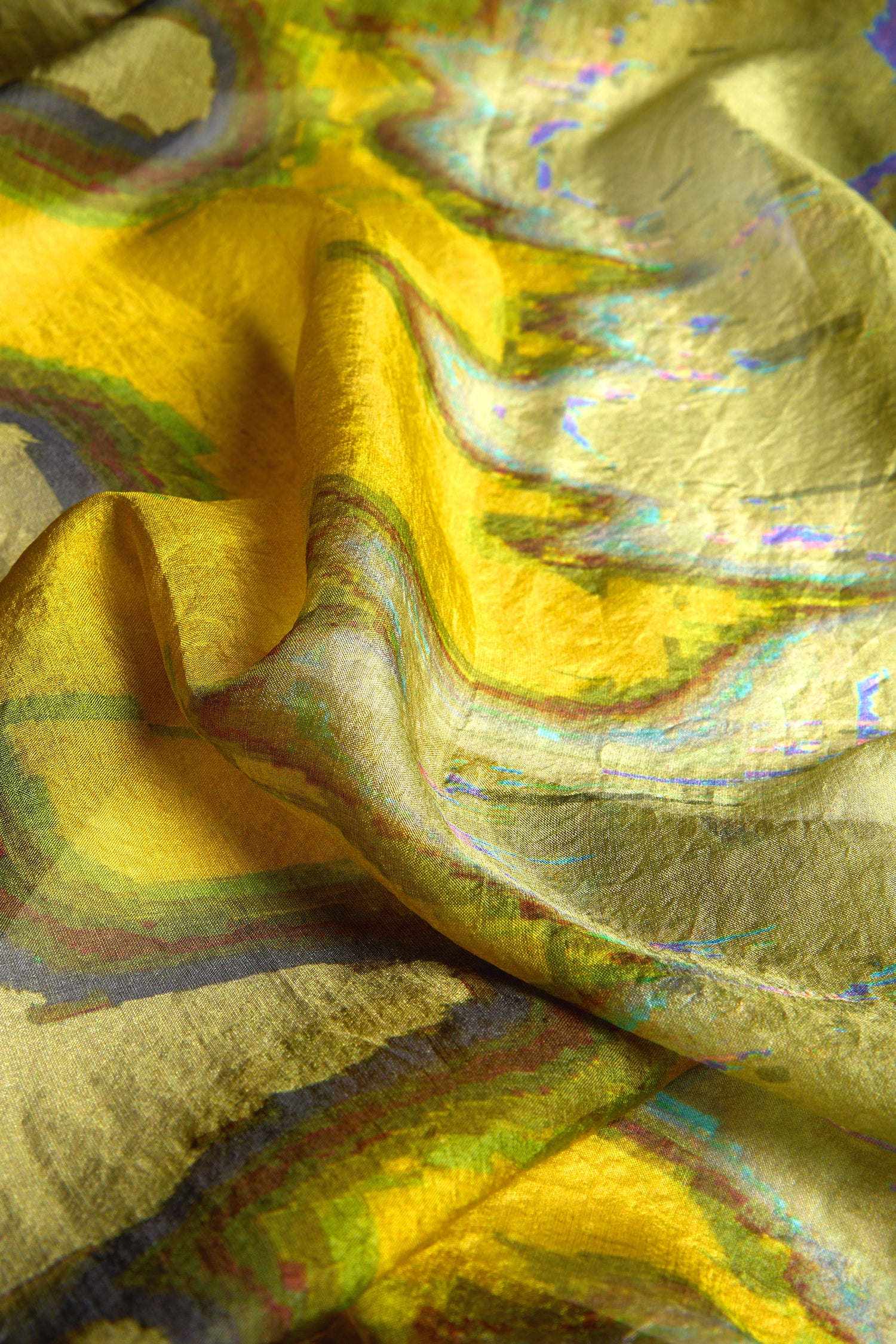 A close-up of a crumpled, yellow and multicolored iridescent fabric displays a shimmering effect and textured surface, evoking the refined luxury of the Mineral Silk Scarf.