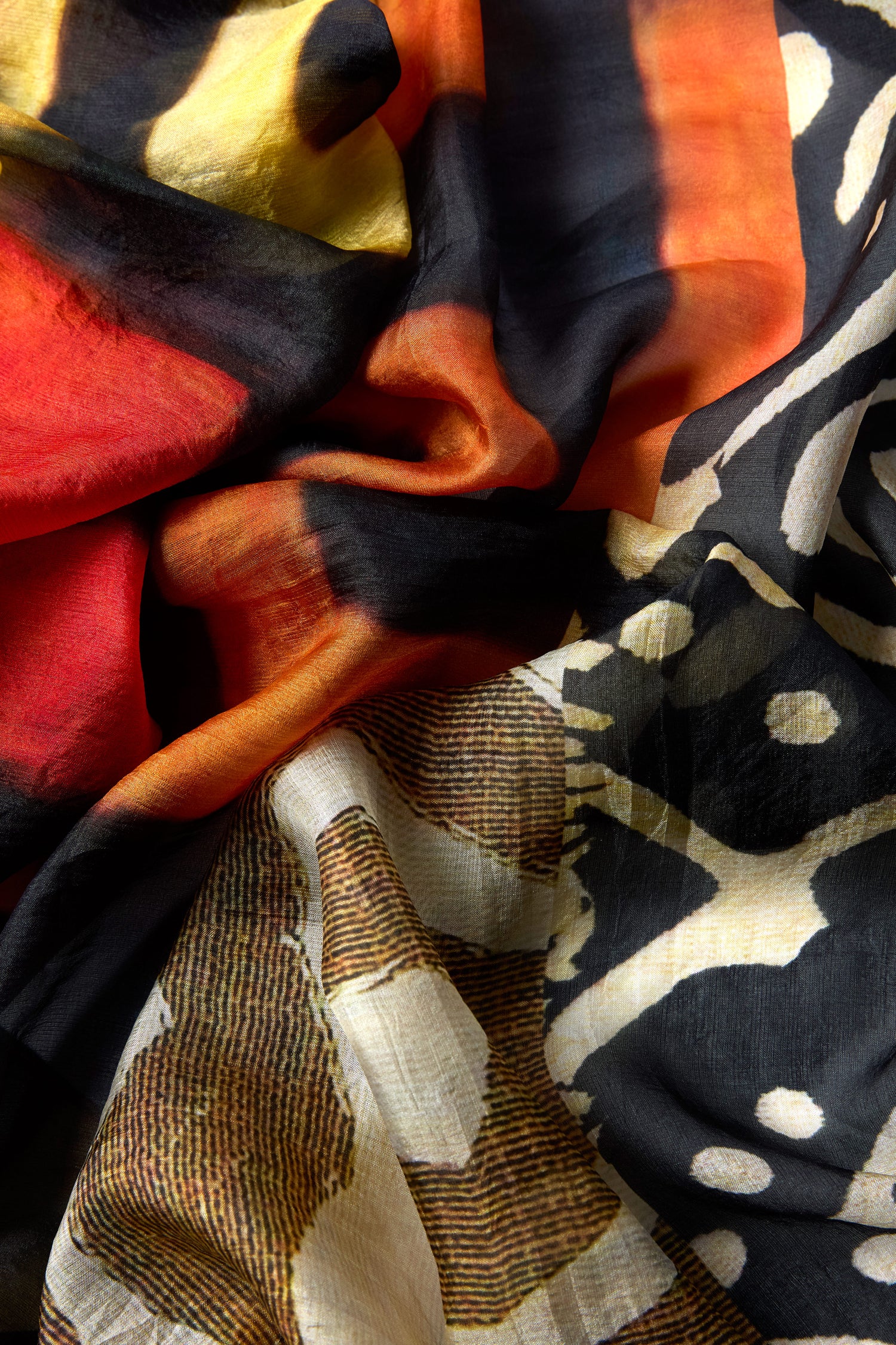 A close-up of the Ancient Silk Scarf, showcasing its colorful tribal-inspired print with abstract designs in red, yellow, black, and white and a soft, lightly crumpled silk texture.