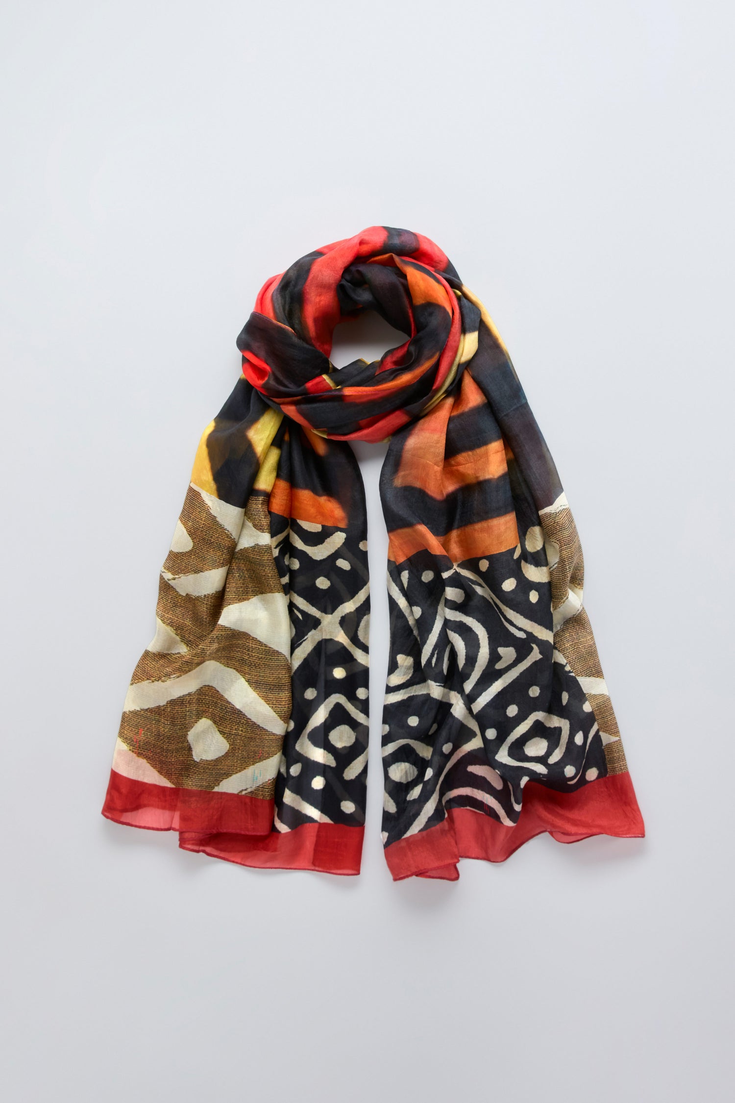 The Ancient Silk Scarf showcases black, yellow, brown, and red tribal-inspired prints in a modern design, displayed flat on a light gray background.