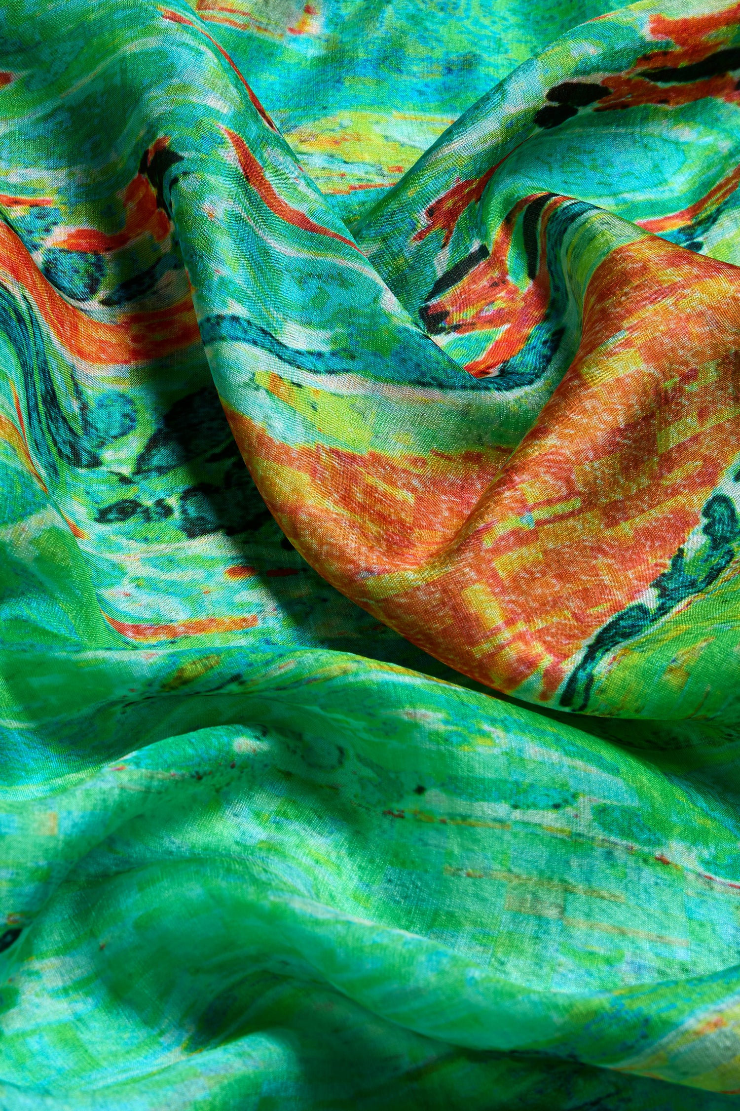 Close-up of the Meadow Silk Scarf, made from pure silk, featuring green, orange, yellow, and black abstract prints. The scarf is softly draped and lightly wrinkled.