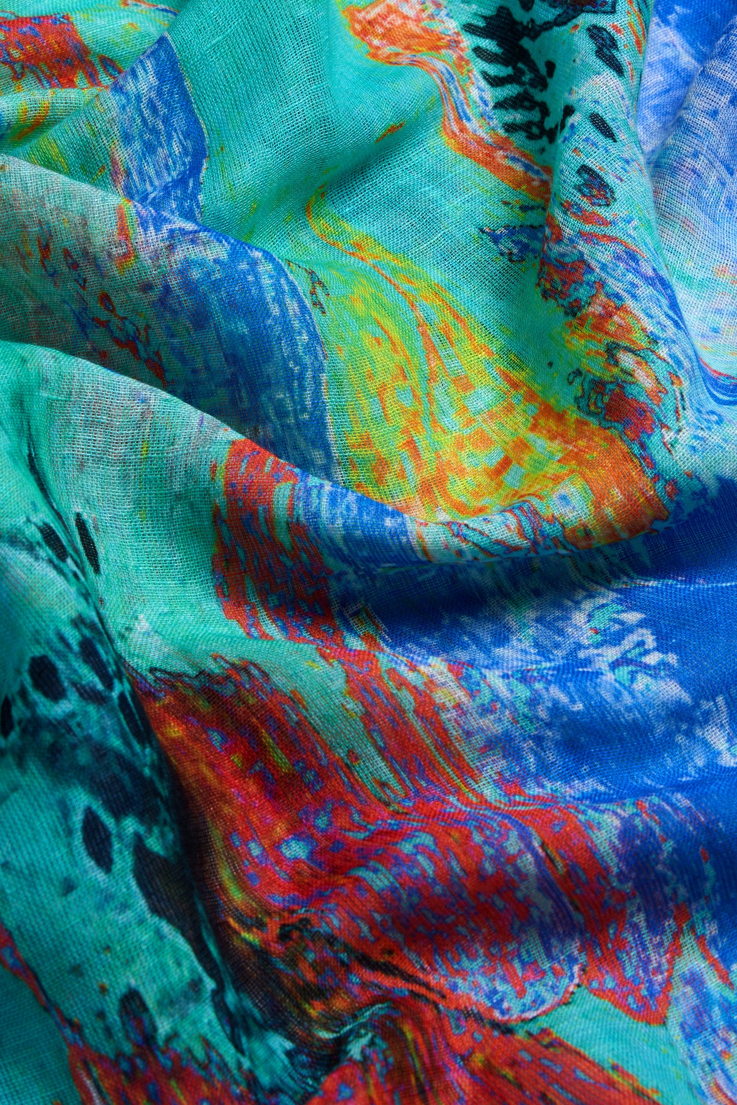 A close-up of the Terra Mare Cotton Linen Scarf highlights its colorful abstract print in blue, green, yellow, red, and black with soft folds and a textured surface.
