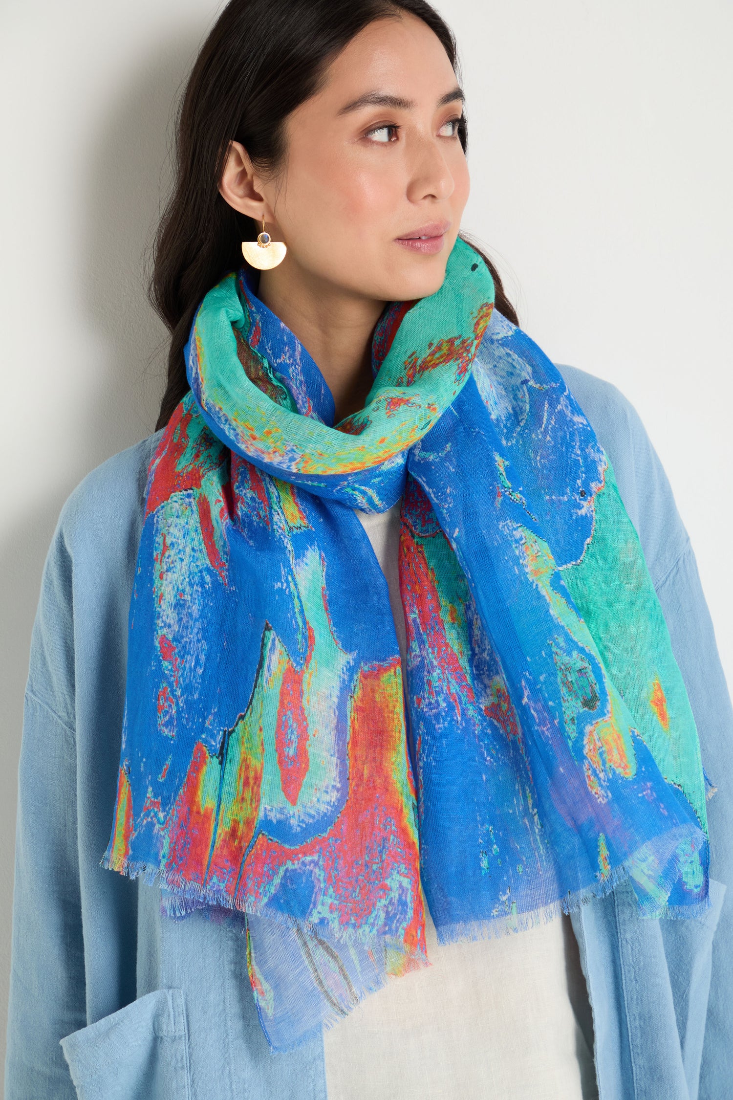 A woman wearing a light blue jacket and the Terra Mare Cotton Linen Scarf looks to the side against a plain background.