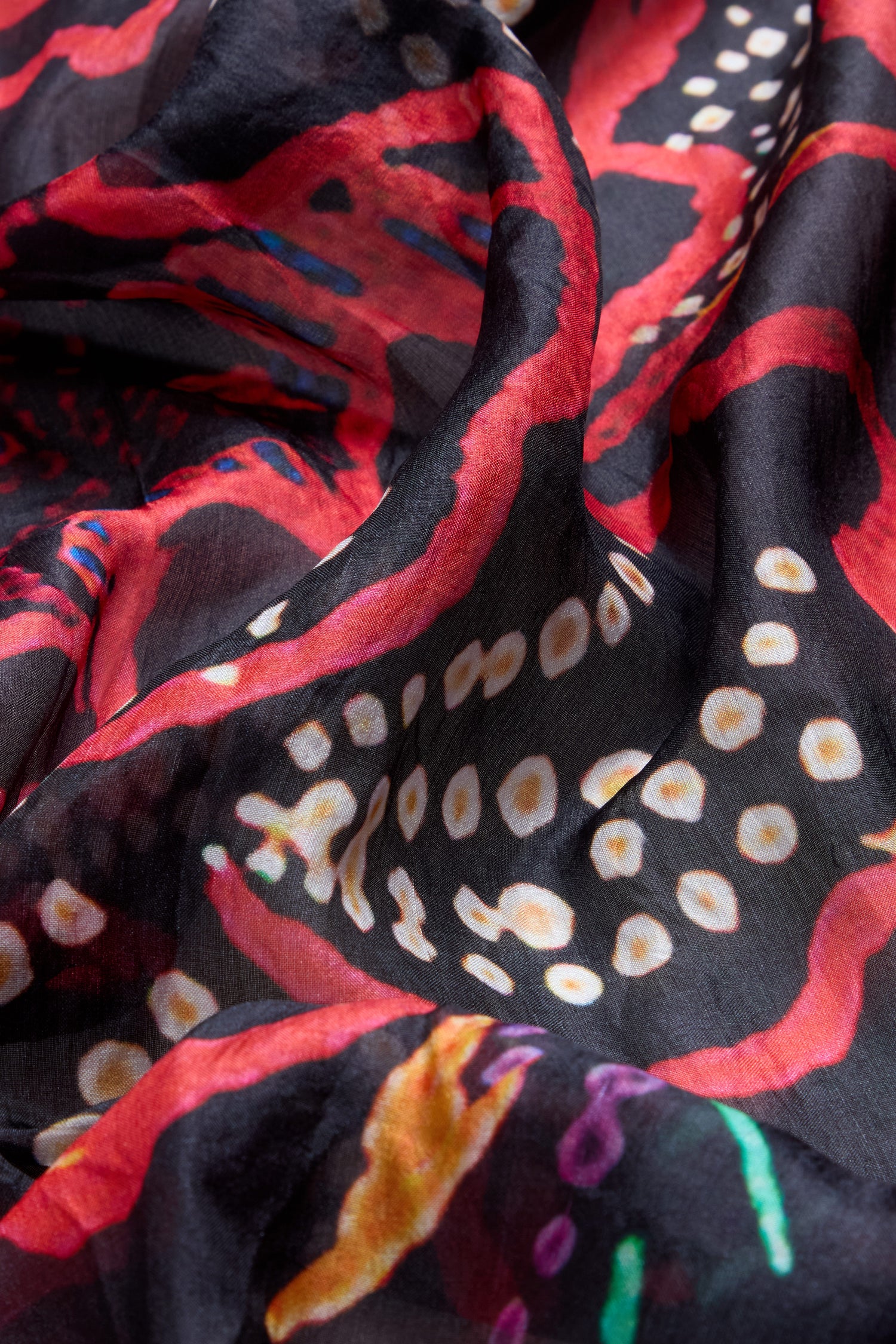 Close-up of the Painted Firework Silk Scarf, a lightweight accessory featuring a colorful abstract print with red, white, orange, and purple shapes on a black background.