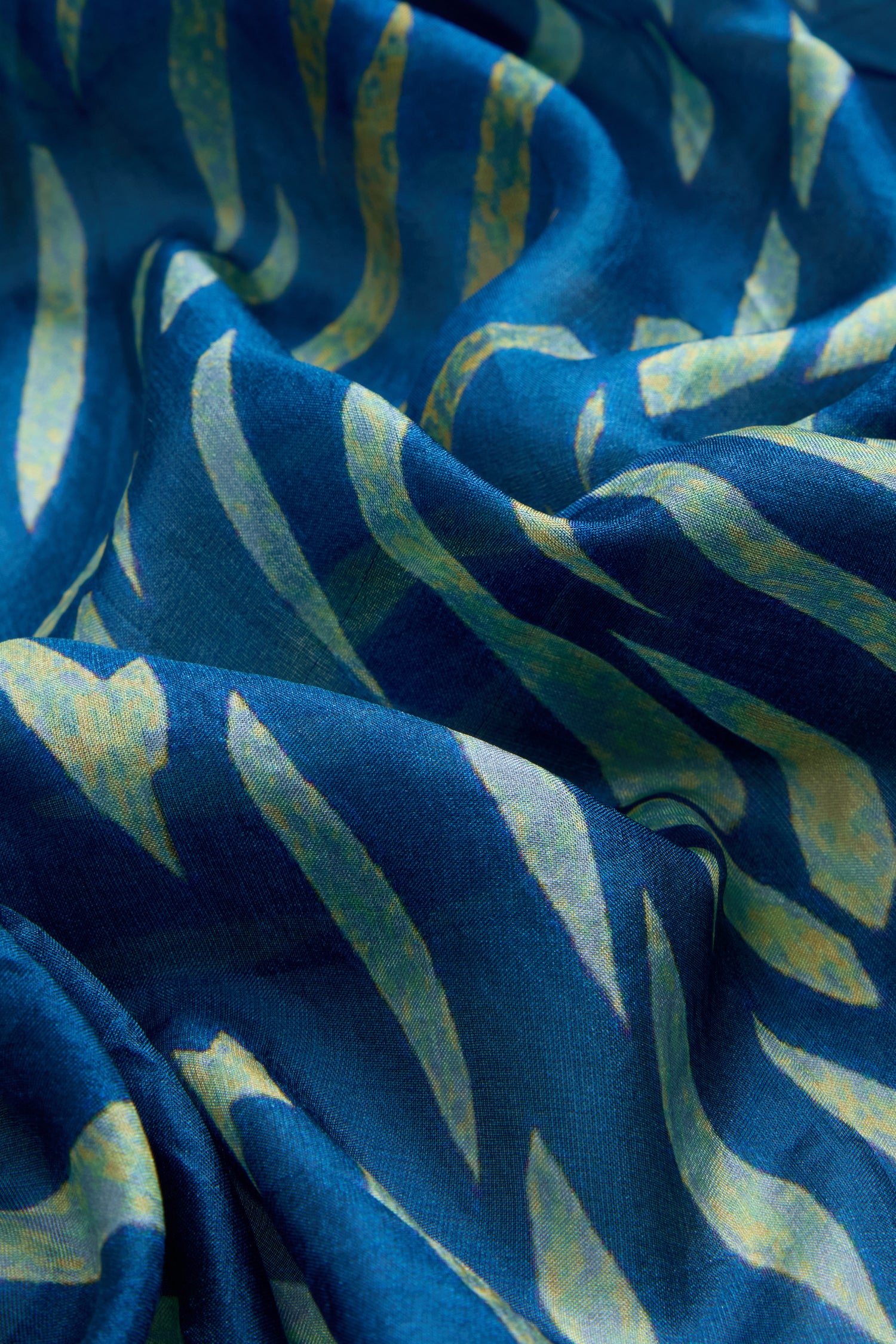Close-up of Painted Waves Silk Scarf in blue with yellow and light blue abstract leaf-like print, highlighting its soft texture and elegant folds.