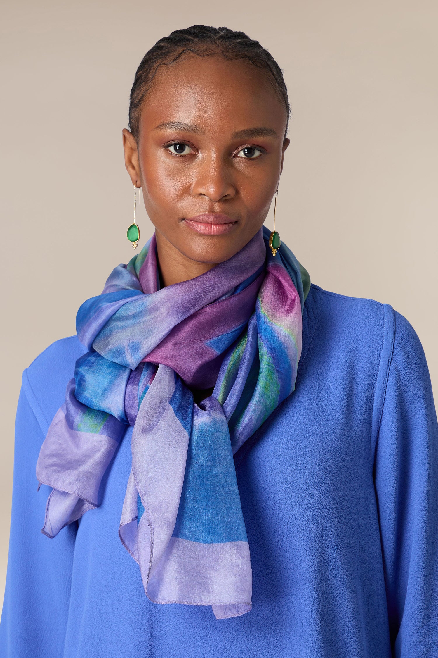 A woman wearing a blue blouse with a vibrant, Lilac Sky silk scarf and green earrings.