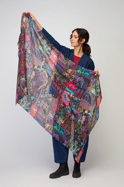A woman in dark clothing displays the Sahara Winter Patchwork Scarf, featuring vibrant colors, against a plain light background.