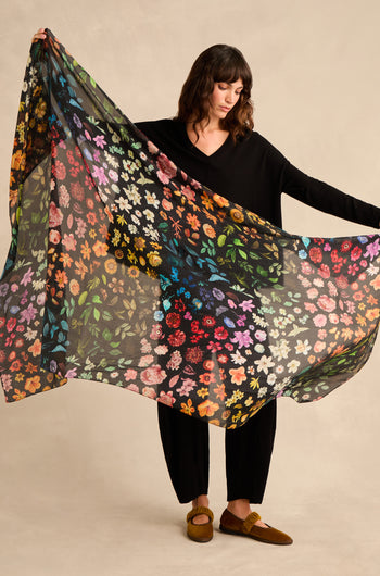 A person dressed in black holds out the Midnight Garden Silk Scarf, showcasing its vibrant botanical print against a neutral background.