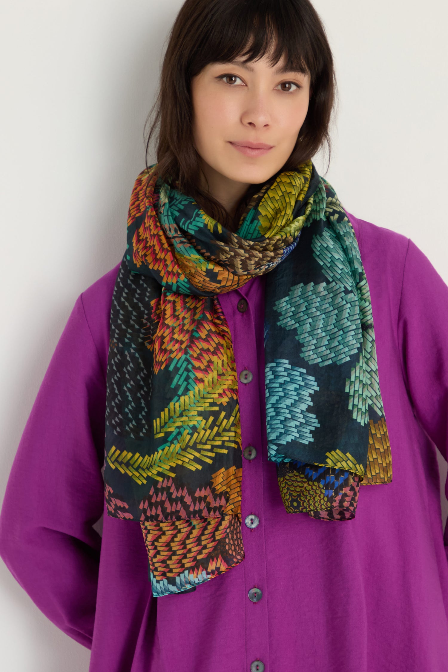 A person wearing a bright purple button-up shirt and the Pixelated Petals Silk Scarf stands against a plain white background.