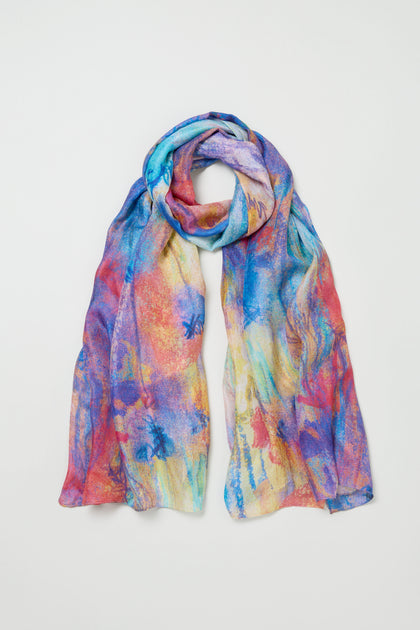 The Soft Meadow Dreams Silk Scarf is lightweight silk with a colorful abstract pattern in blue, pink, orange, and yellow hues, shown laid flat on a white background.